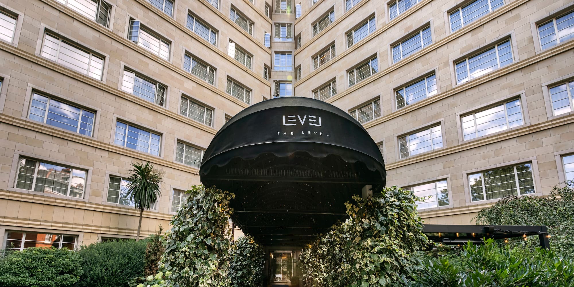 Elegant hotel entrance with 'The Level' awning, lush ivy, and grand building.