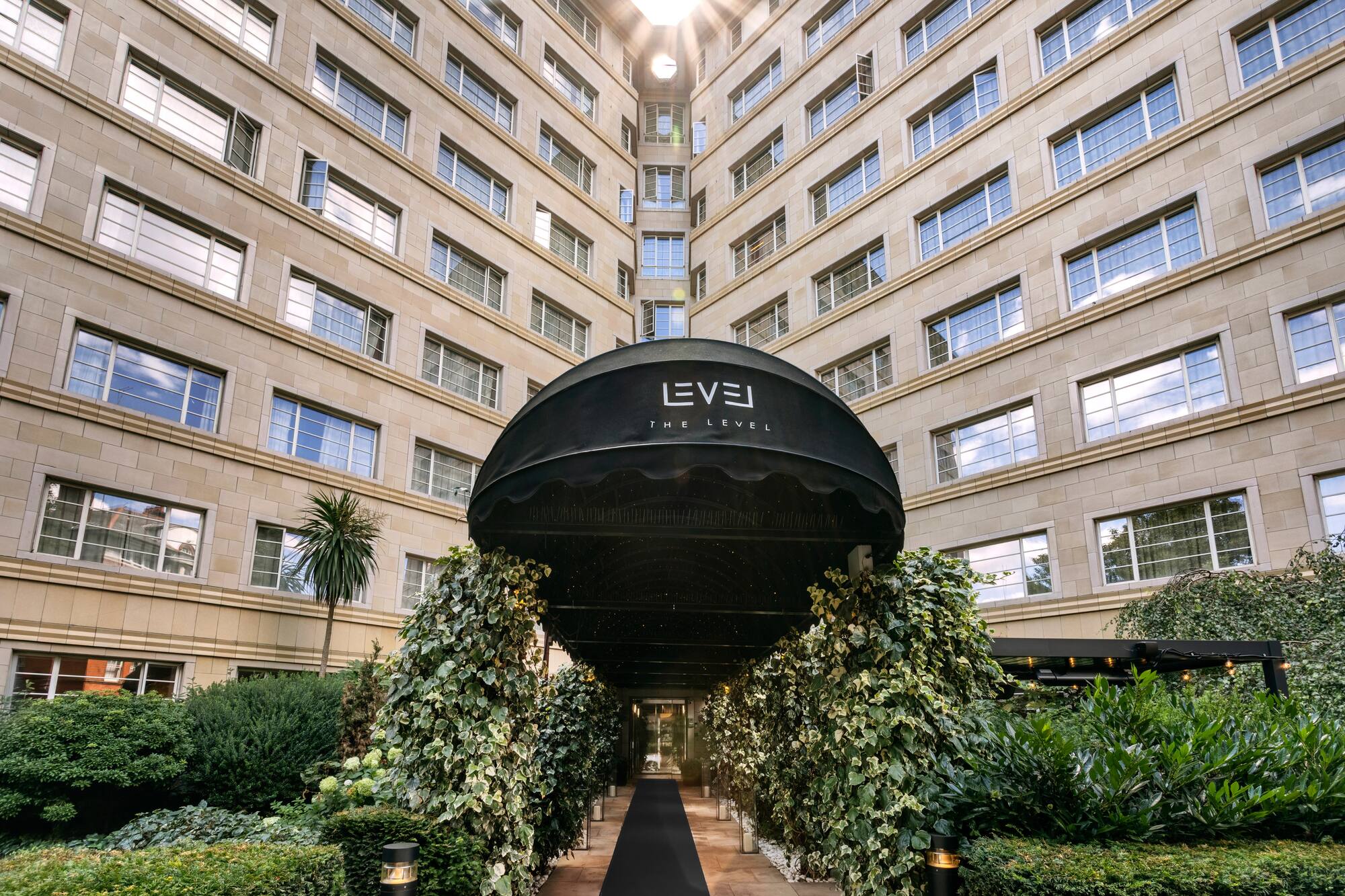 Elegant hotel entrance with 'The Level' awning, lush ivy, and grand building.