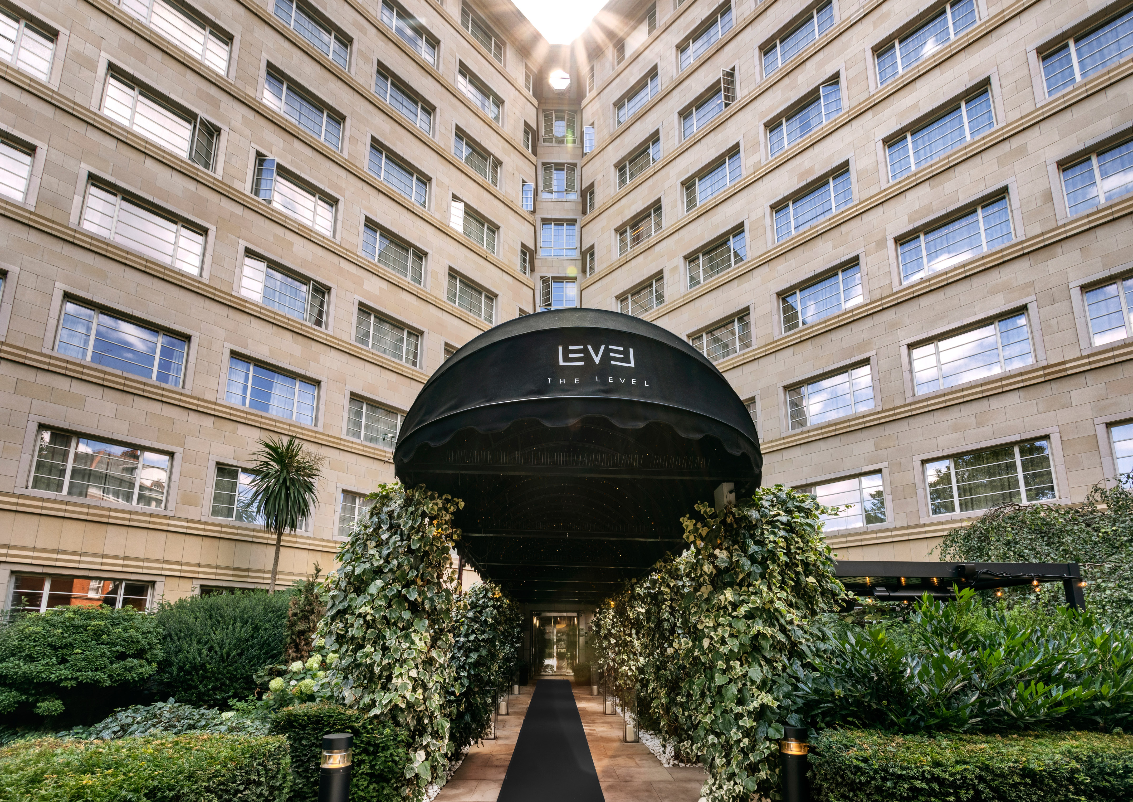 Elegant hotel entrance with 'The Level' awning, lush ivy, and grand building.