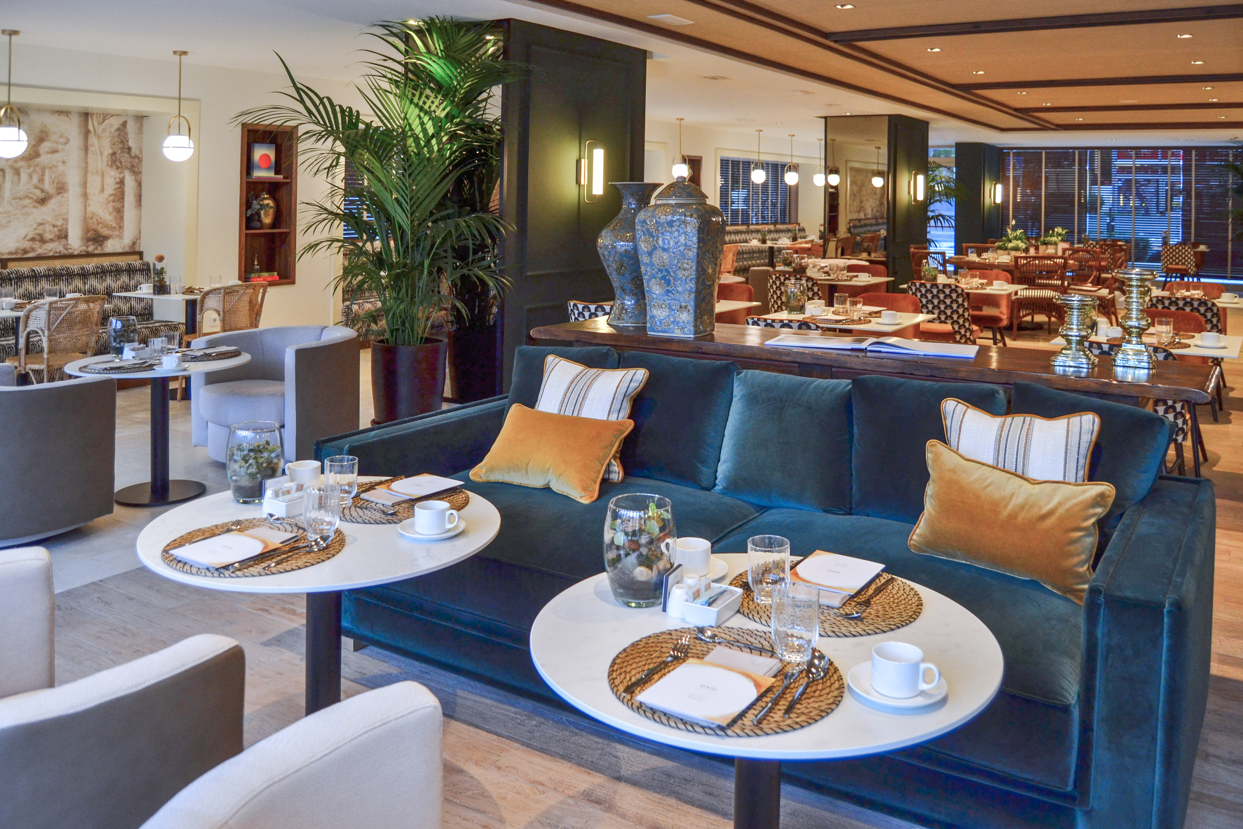 Elegant hotel lounge dining area with teal sofa and set tables.