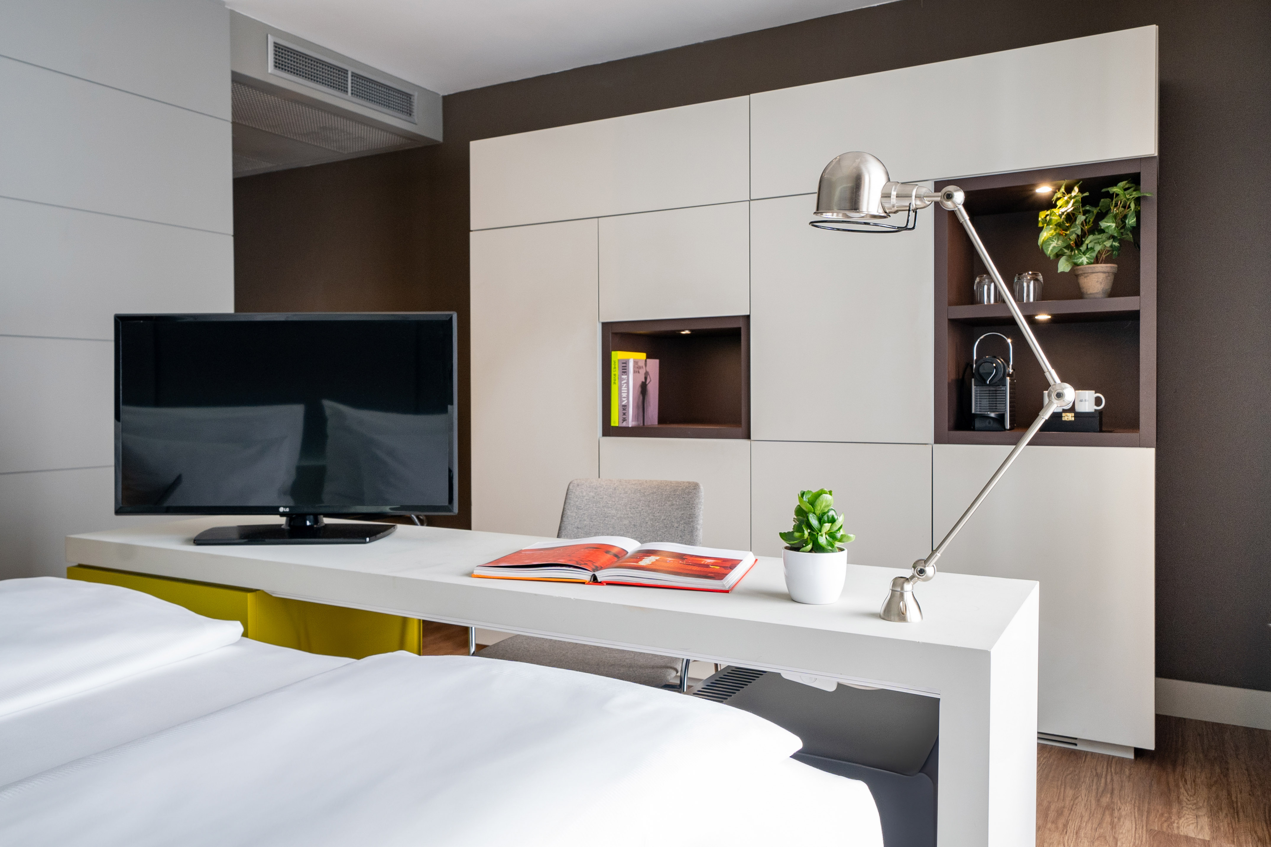 Modern hotel room with TV, workspace, bed, and integrated storage cabinet.