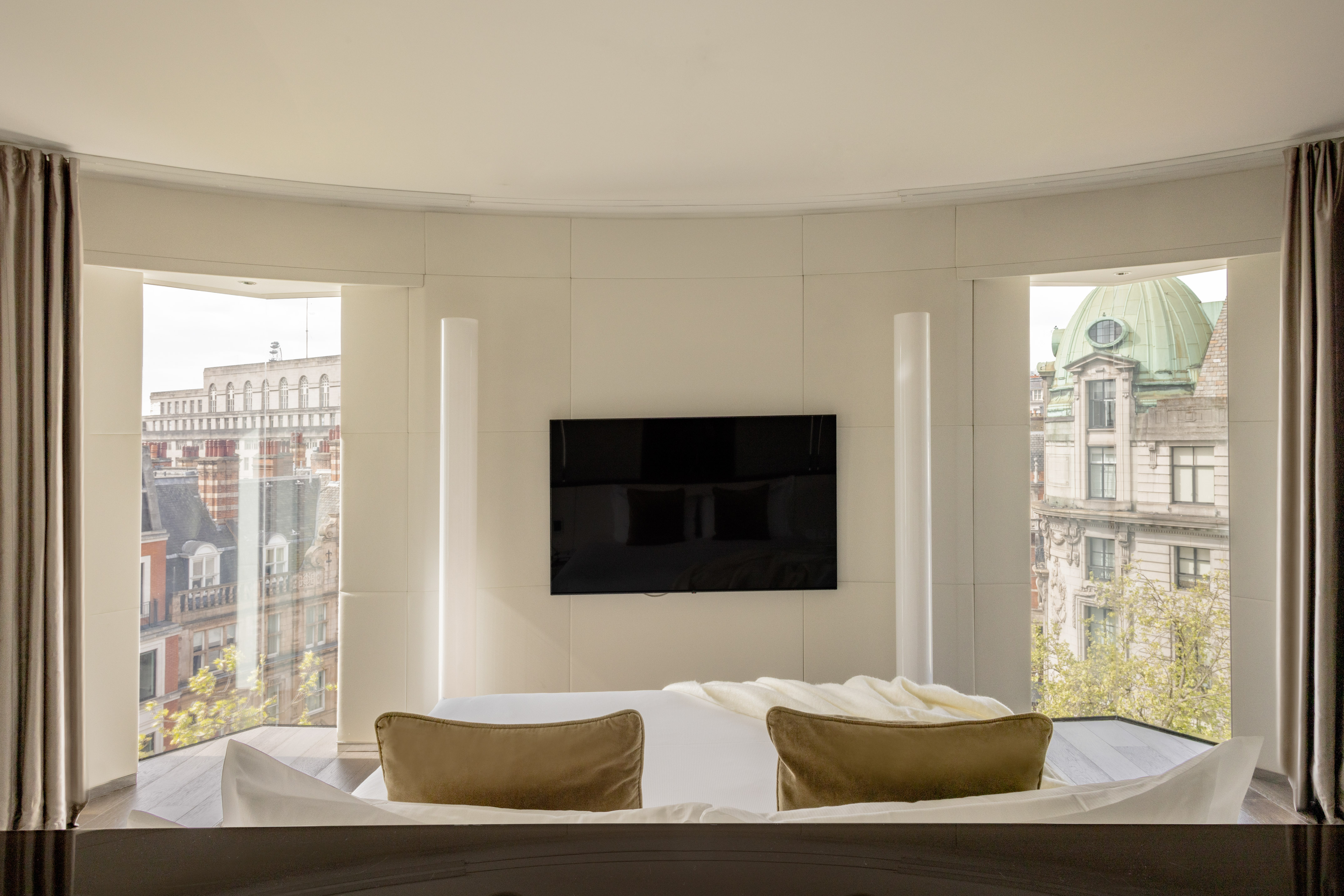 Modern hotel bedroom with curved panoramic windows, city view, and wall TV.
