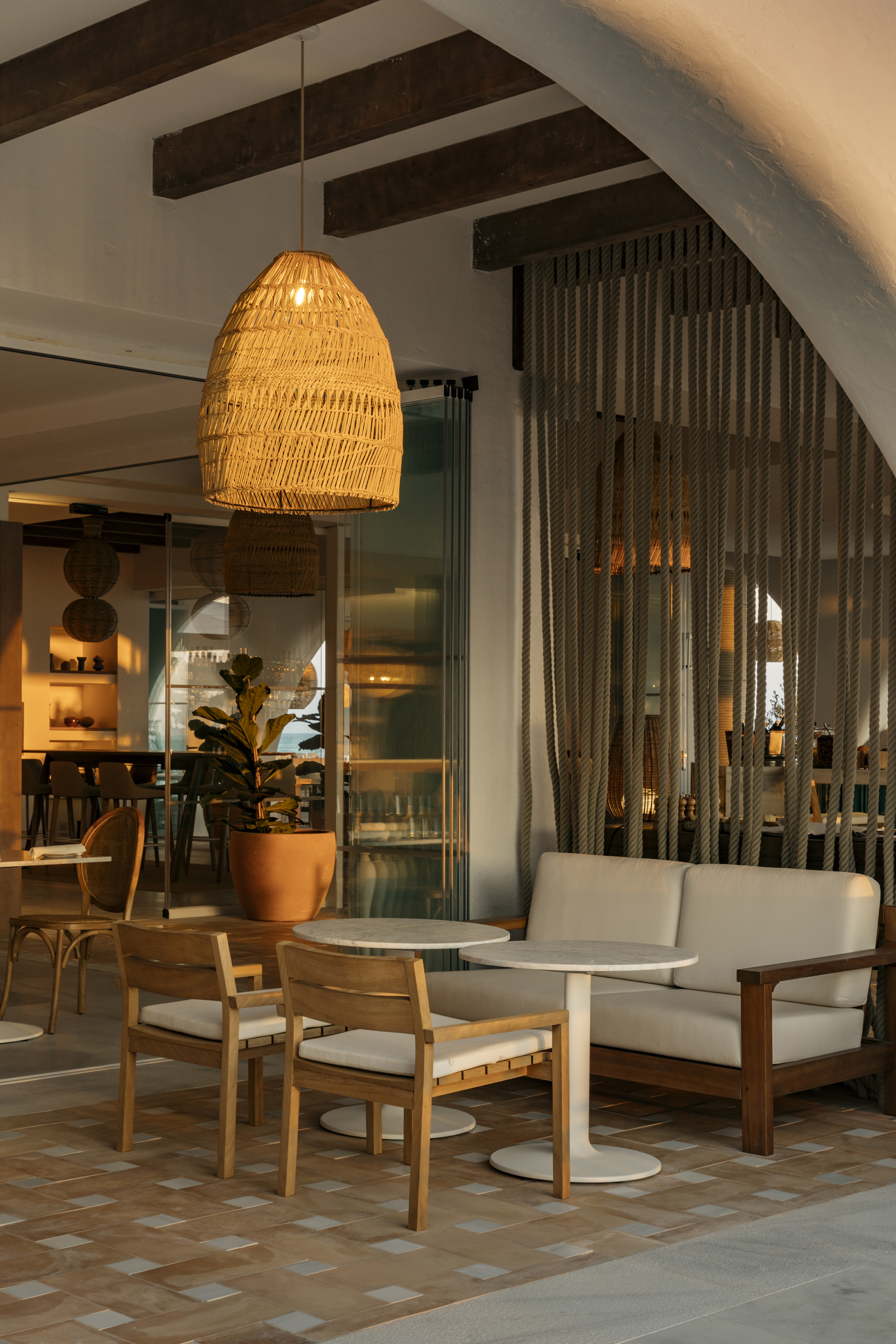 Cafe patio with woven wicker light, wooden seating, and rope divider.