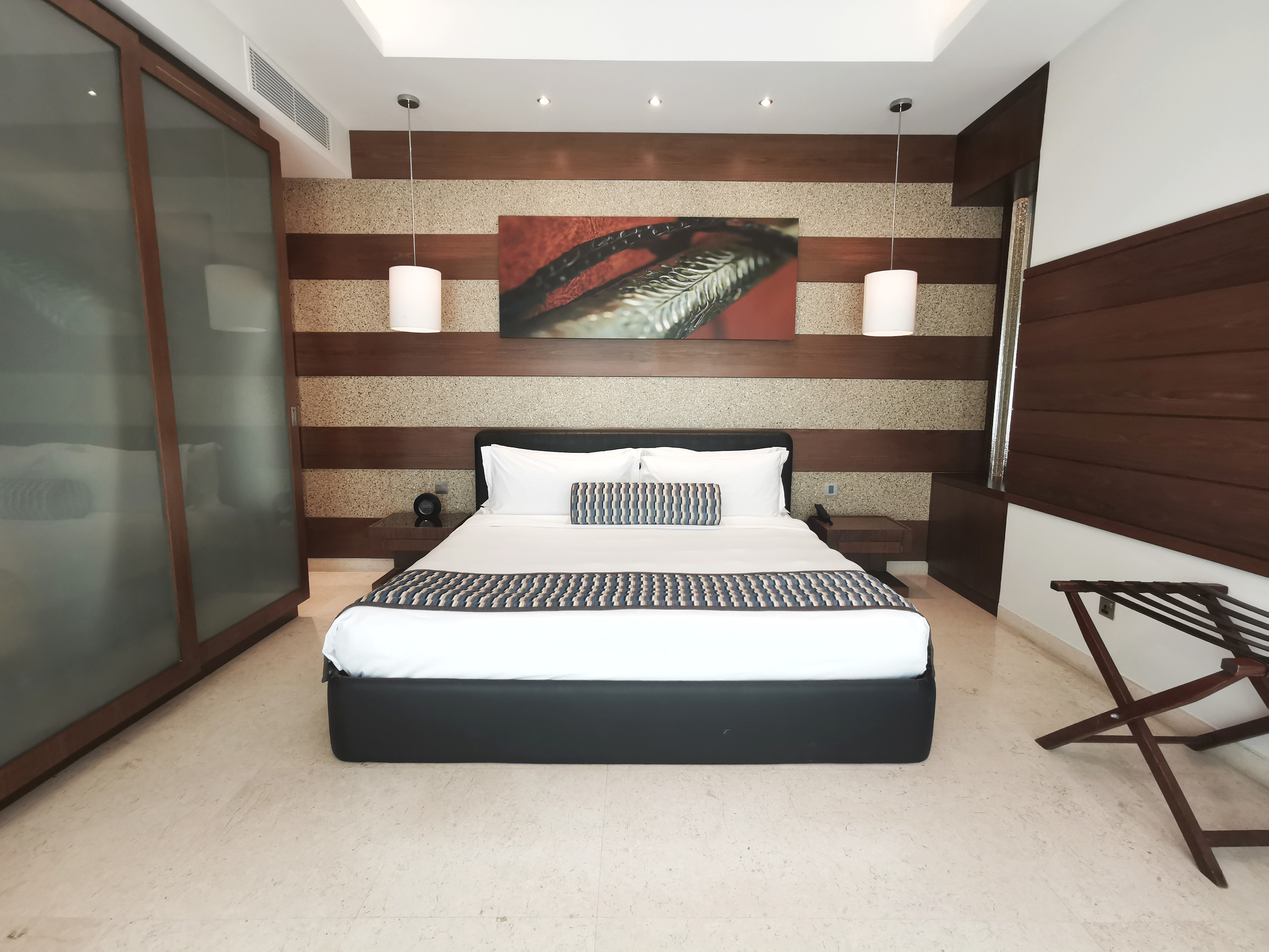 Luxury hotel room with large bed, wooden accent wall, and abstract art.