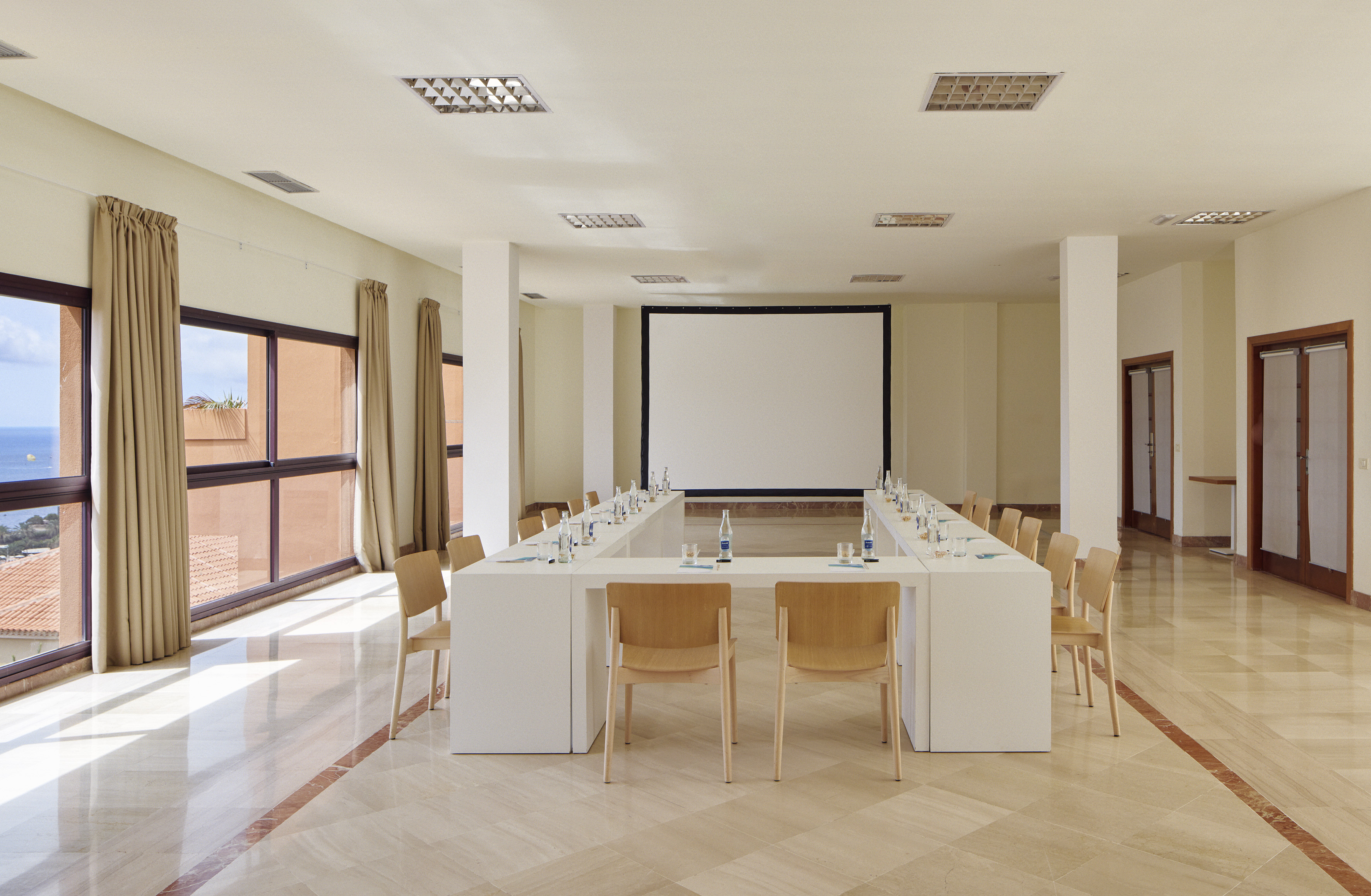 Modern conference room with U-table, projector screen, and ocean view windows.