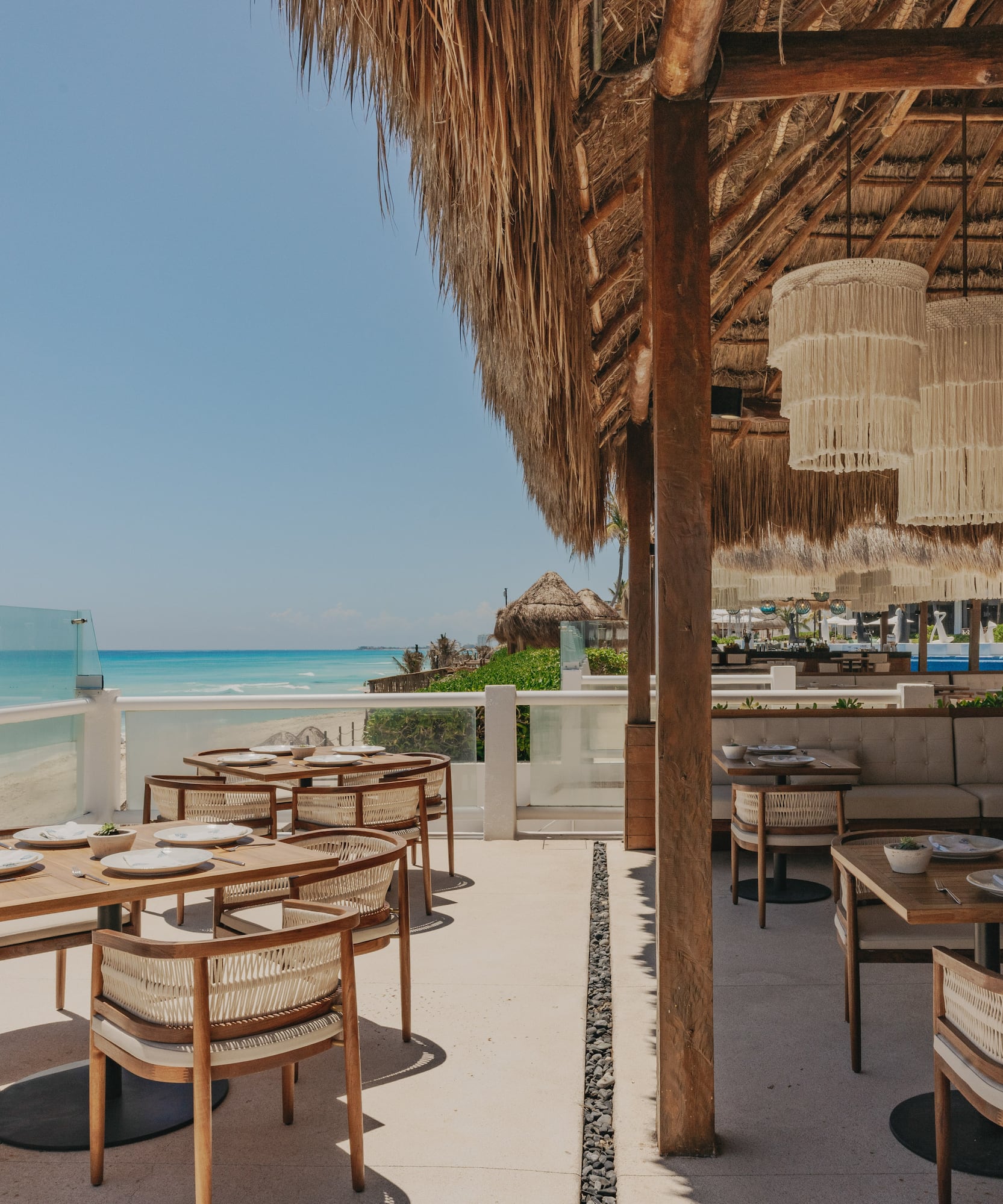 Beach restaurant patio with ocean view, thatched roof, and macrame lighting.