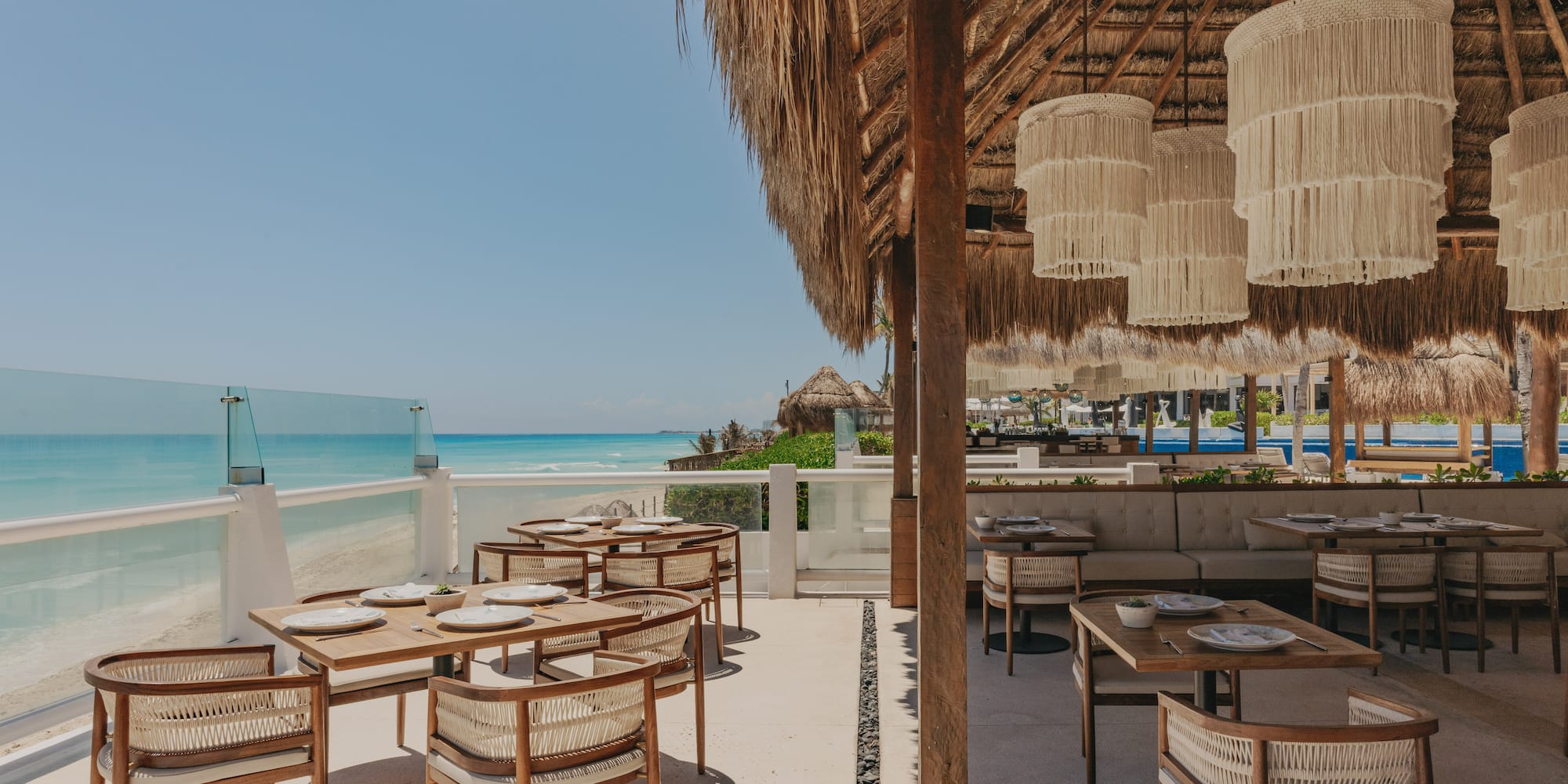 Beachside restaurant under a thatched roof with ocean view and stylish tables.