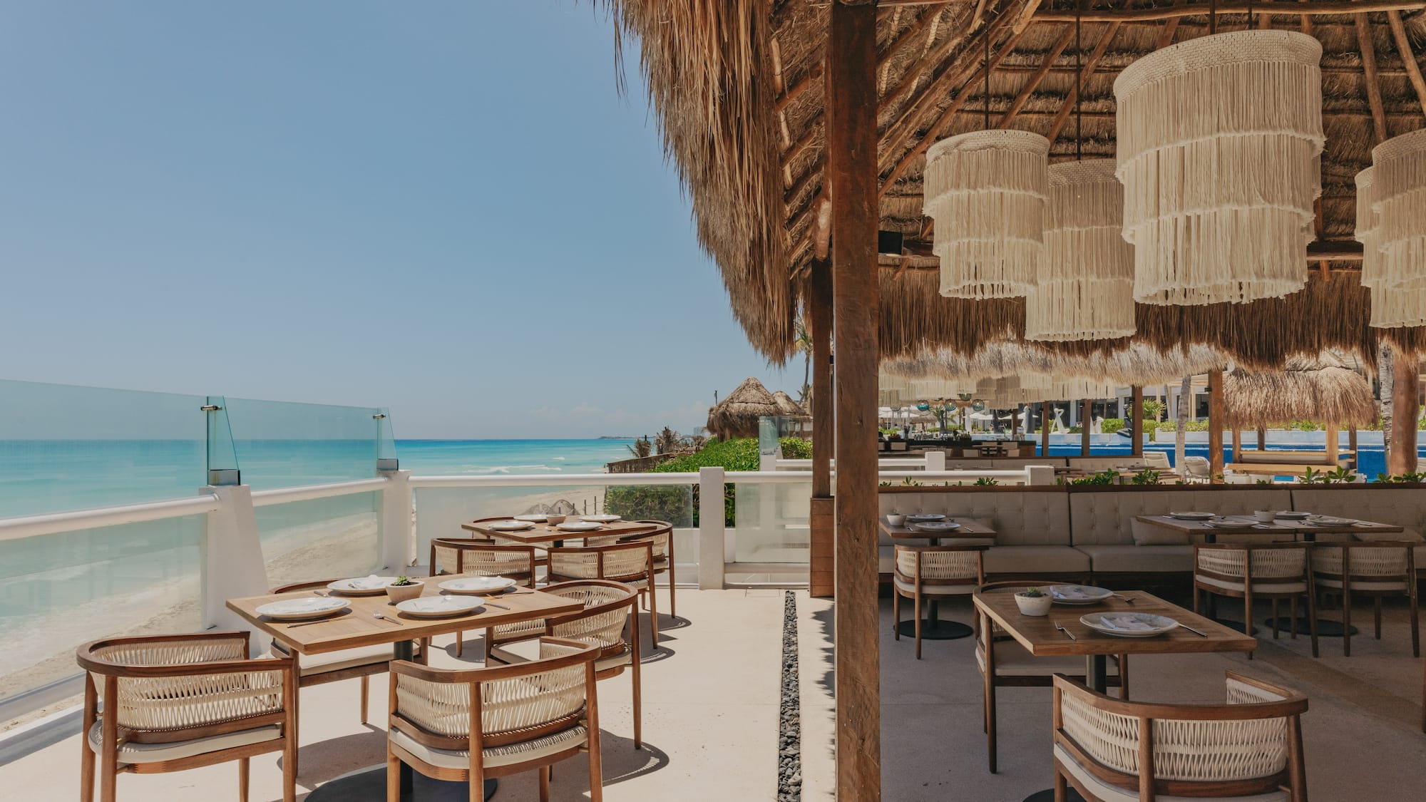 Beachside restaurant under a thatched roof with ocean view and stylish tables.