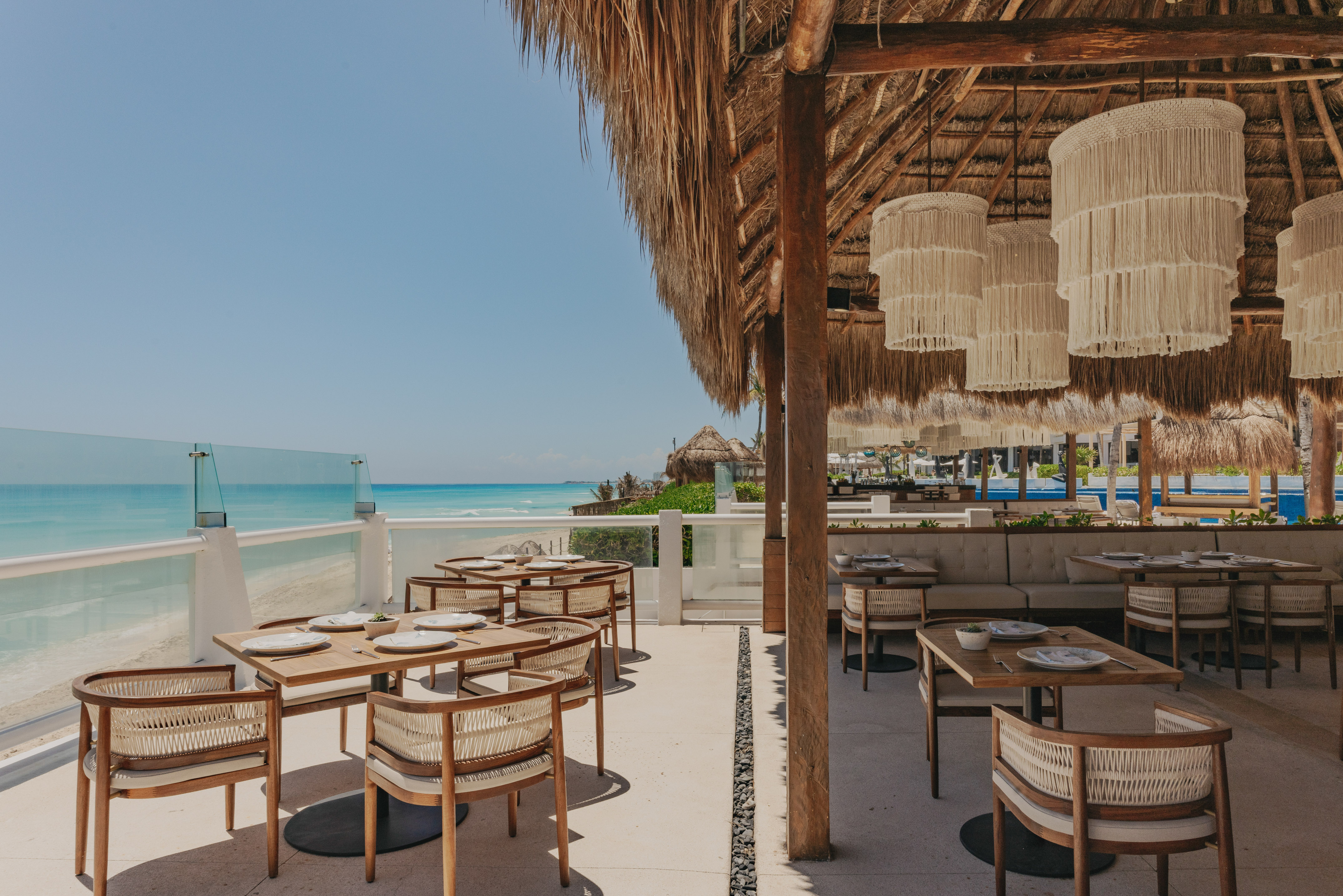Beachside restaurant under a thatched roof with ocean view and stylish tables.