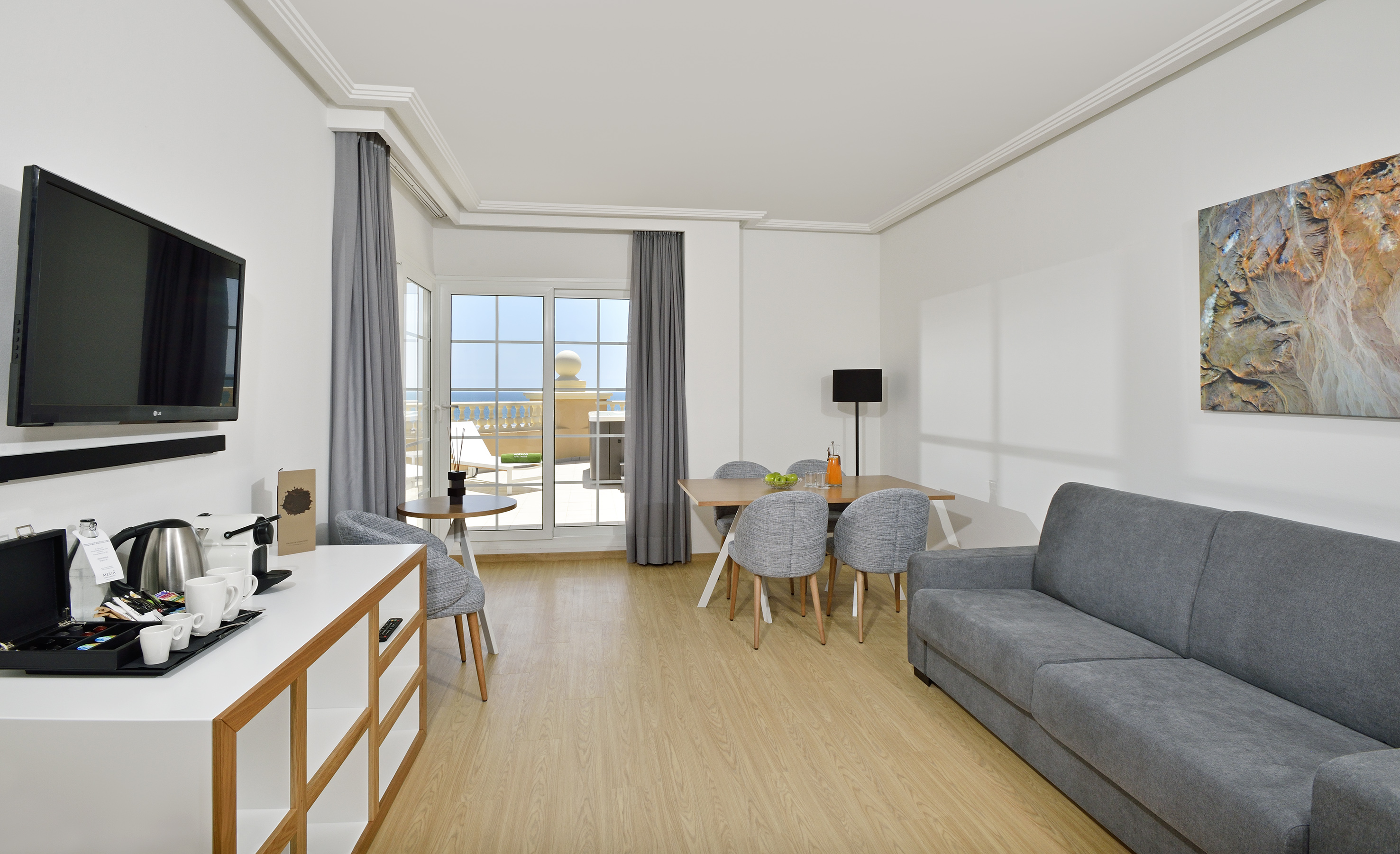 Modern hotel living room suite with sea view balcony and dining area.