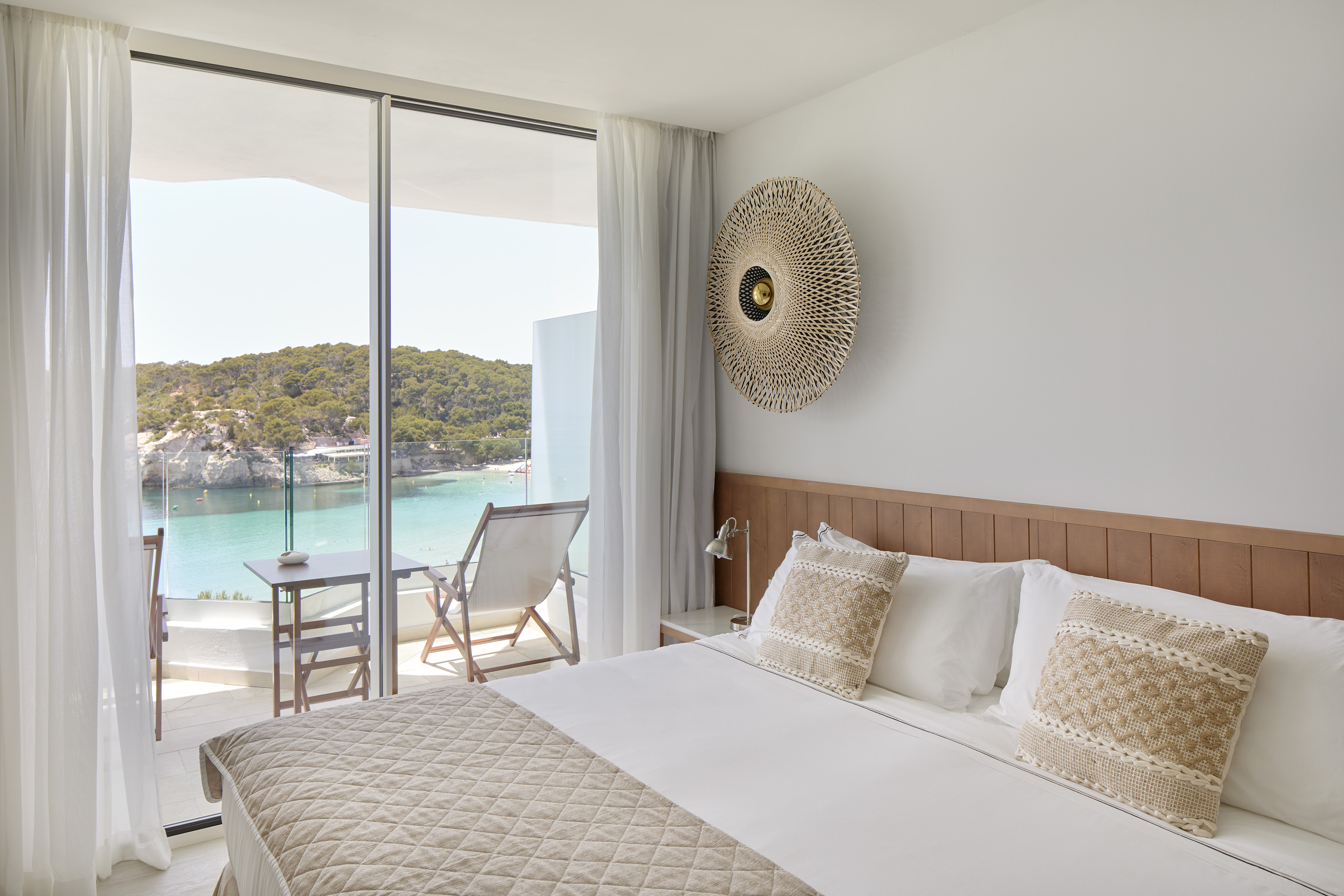 Coastal hotel bedroom with balcony, turquoise sea and beach view.
