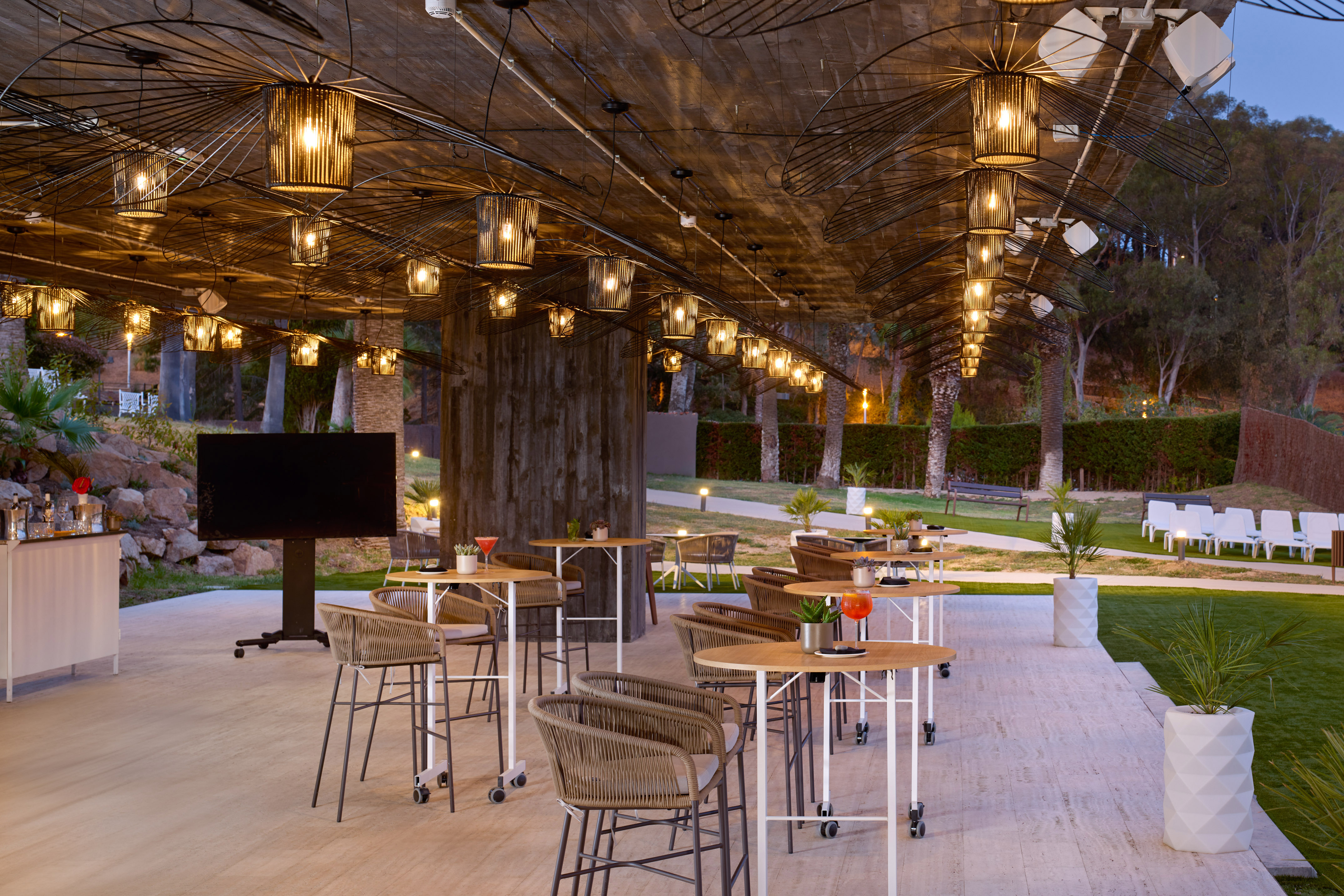 Outdoor bar with unique lighting fixtures, modern high tables, and cocktails at night.