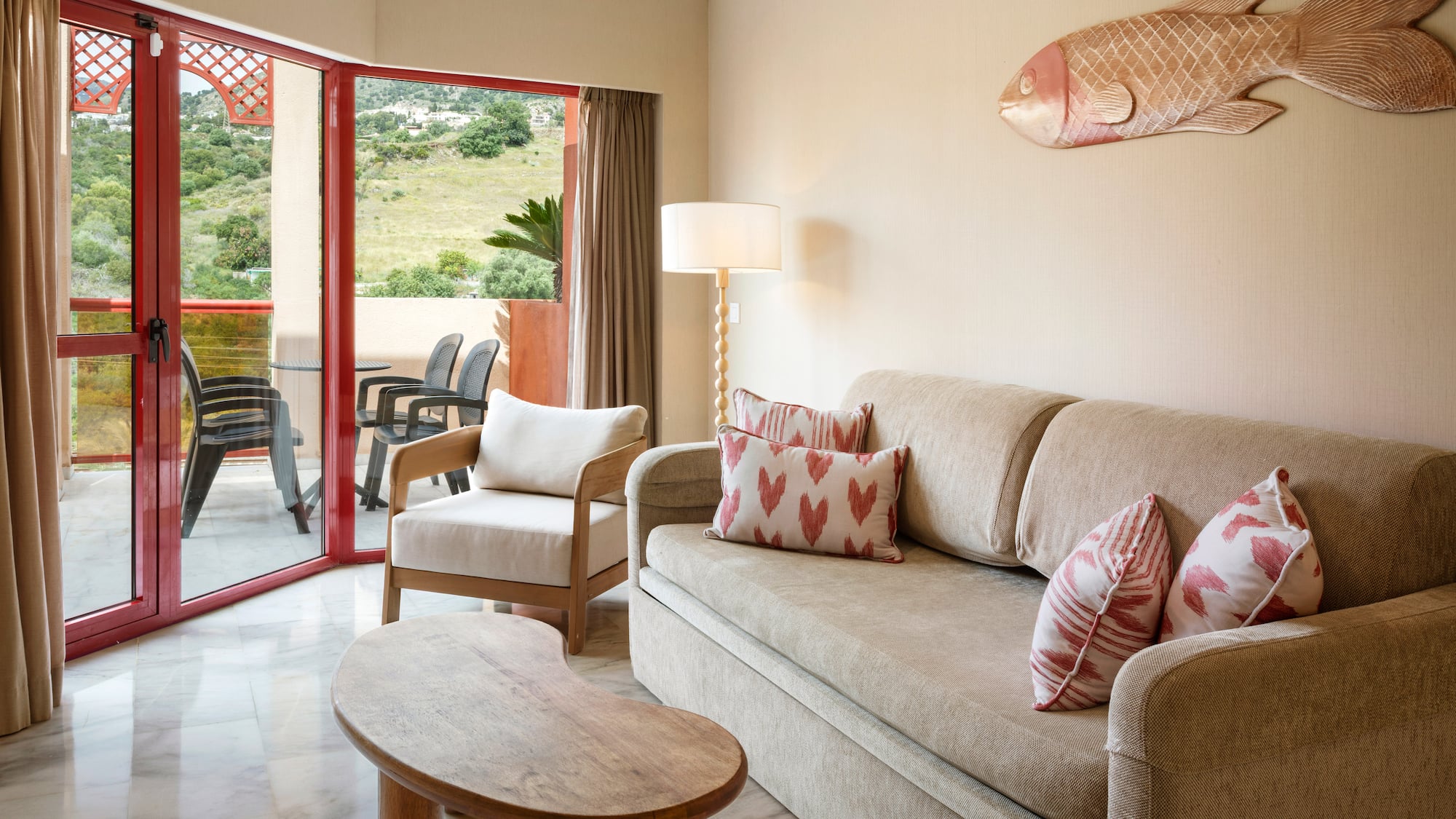 Hotel suite living room with sofa, armchair, balcony, and lush green views.