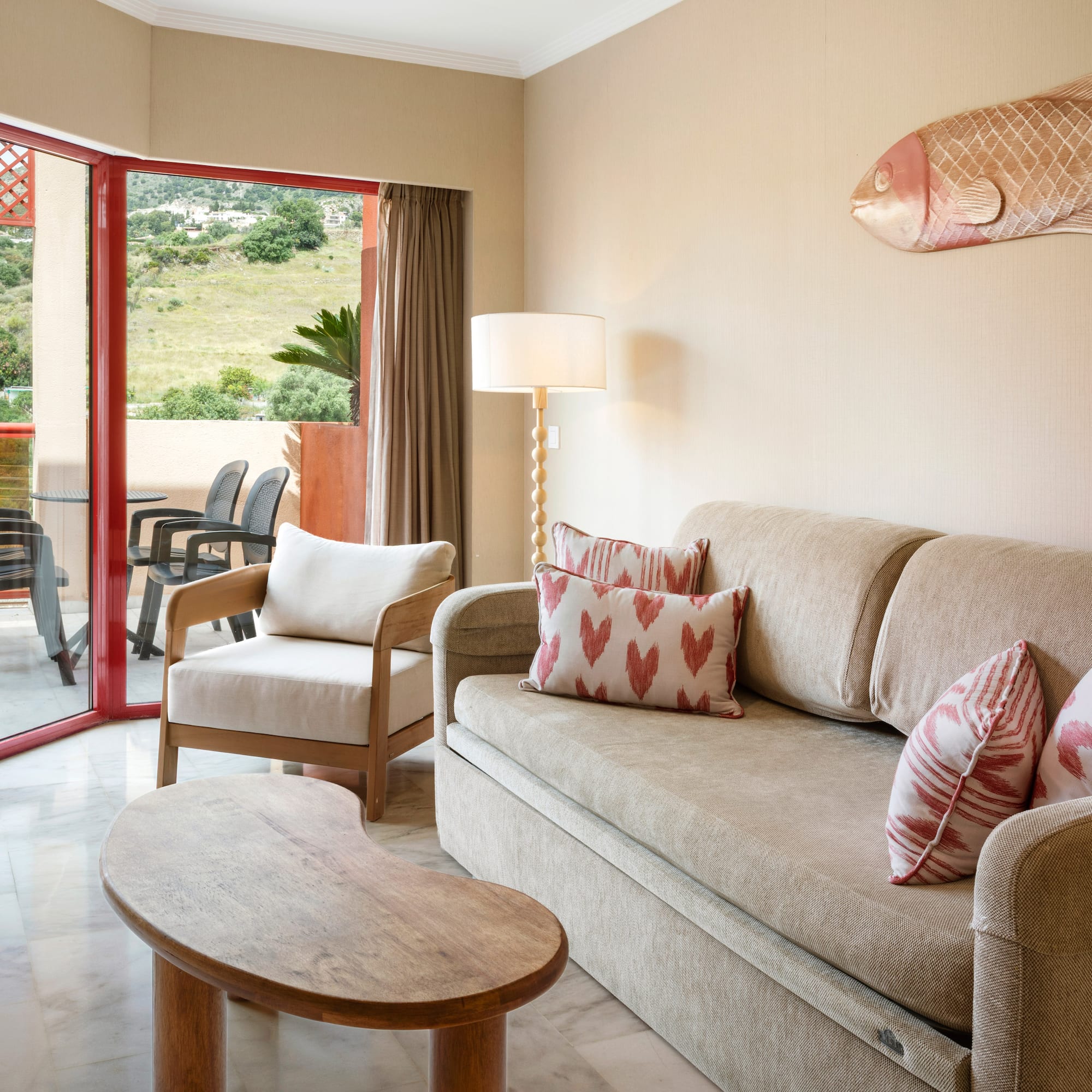 Hotel living room with sofa, armchair, and balcony with green hill view.