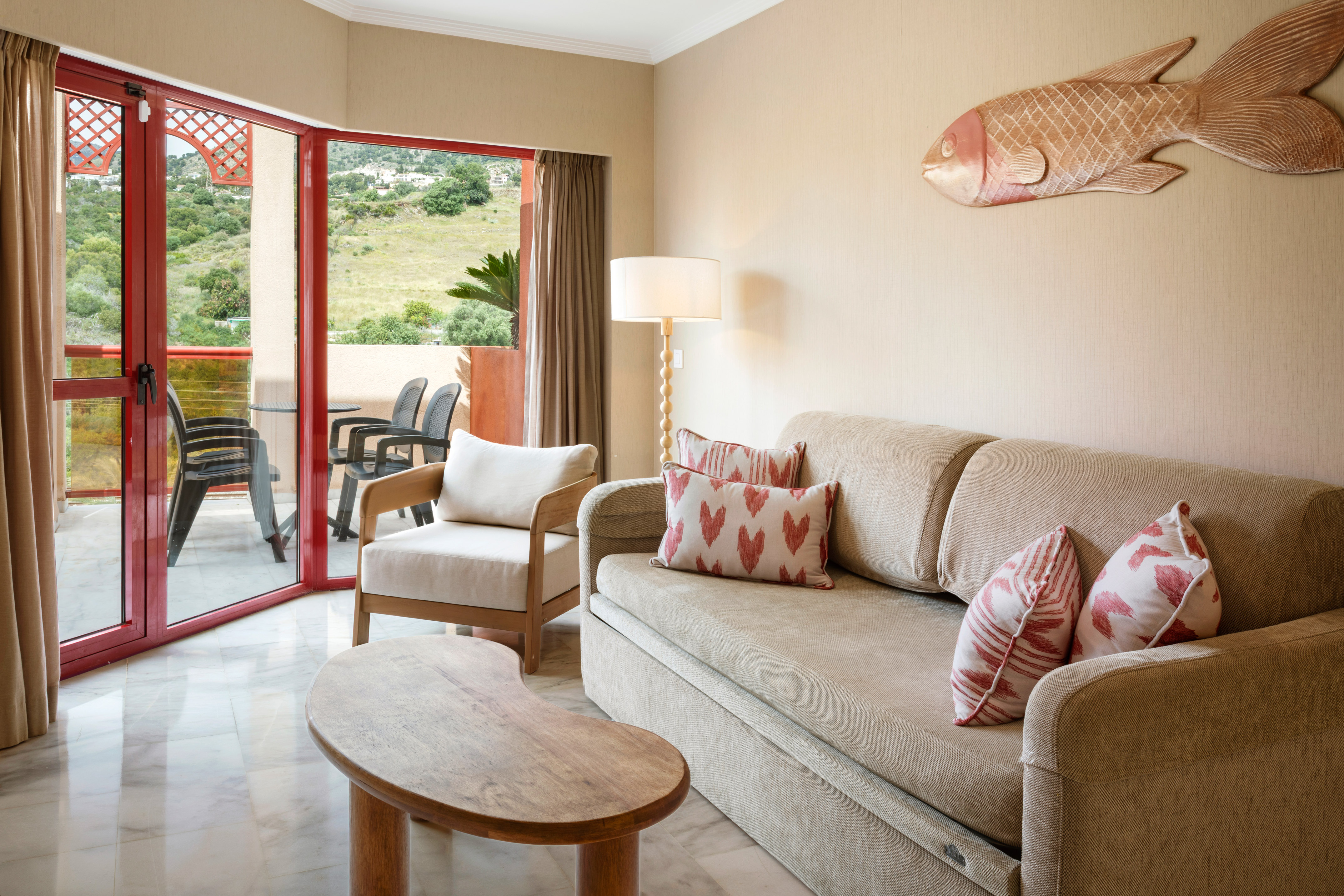 Hotel suite living room with sofa, armchair, balcony, and lush green views.