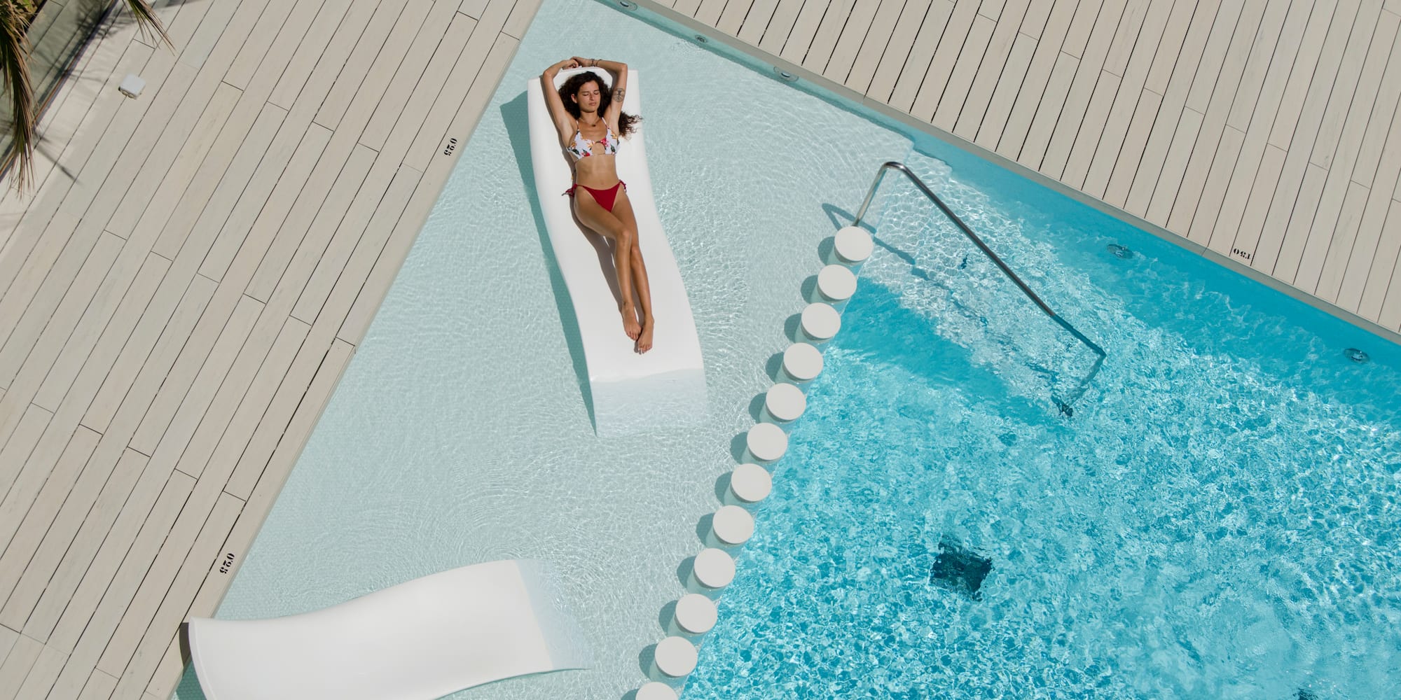 a woman in a garment lying on a floating bed next to a pool