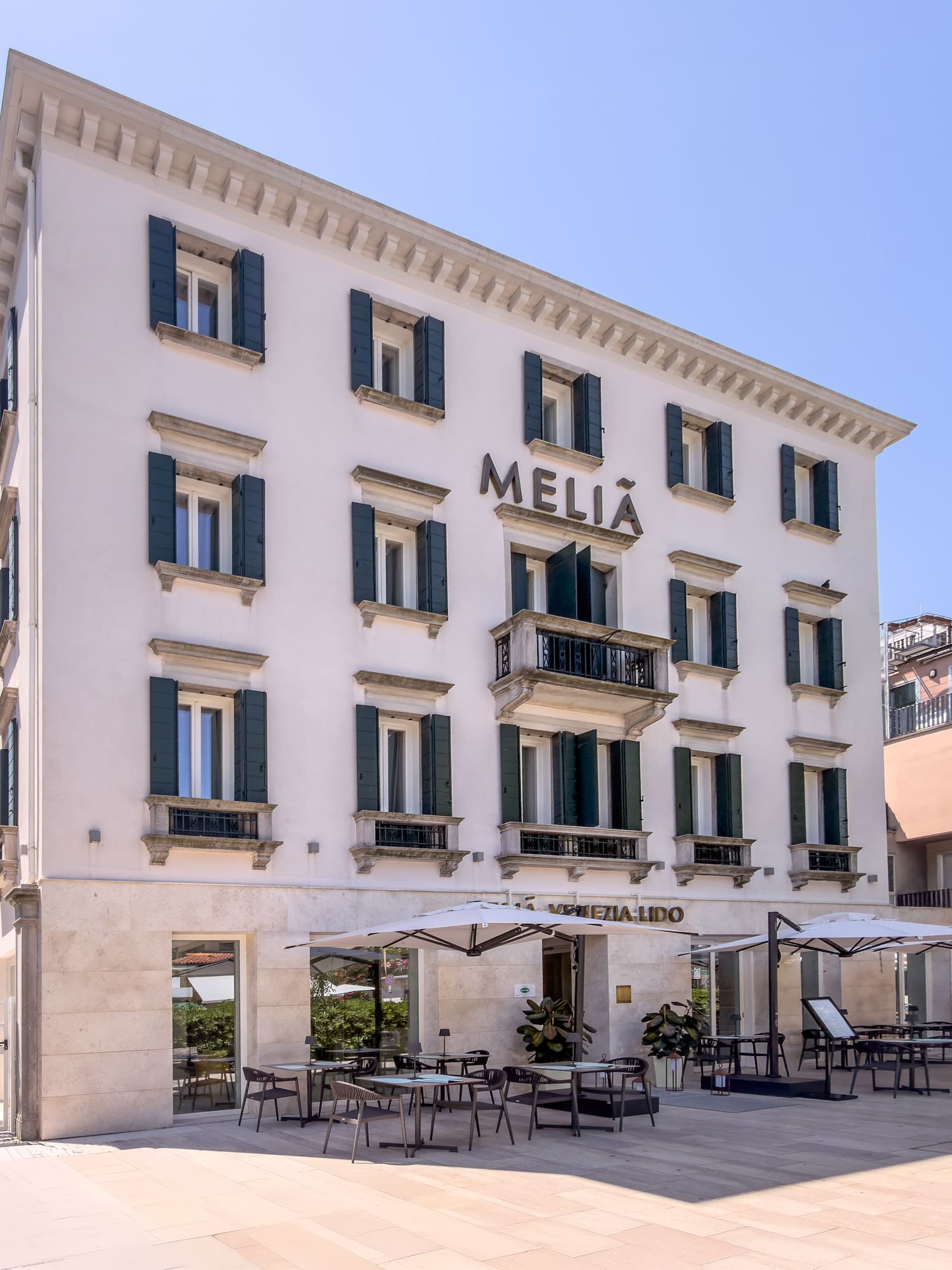 Meliá Venezia Lido hotel exterior, white building, green shutters, outdoor dining.
