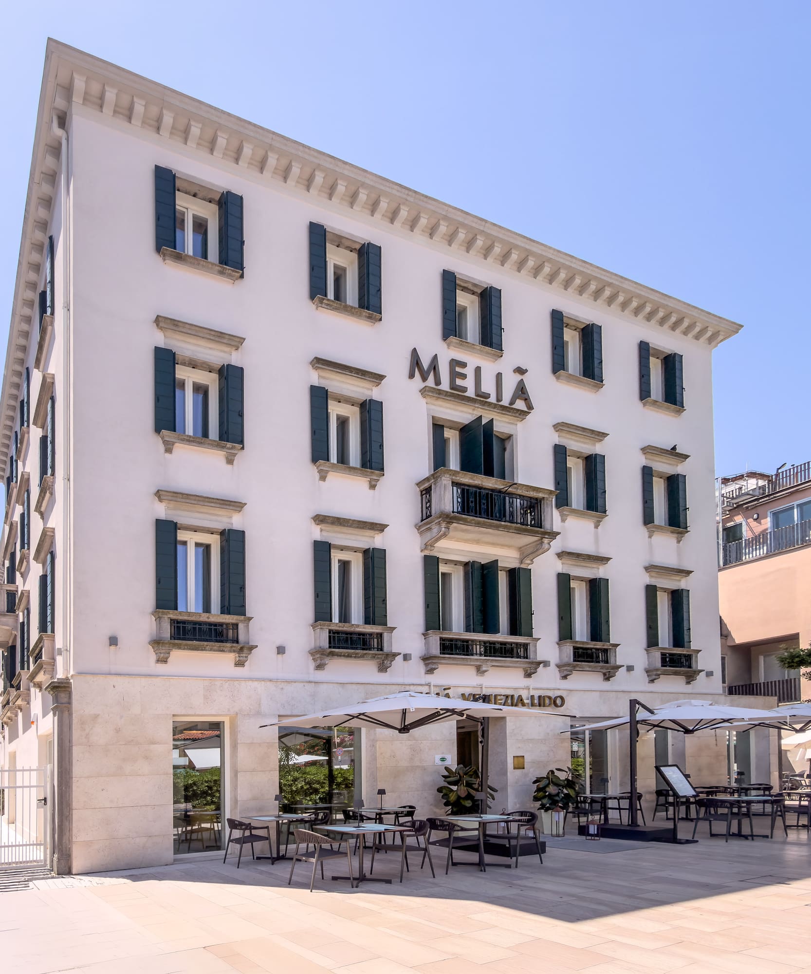 Meliá Venezia Lido hotel exterior, white building, green shutters, outdoor dining.