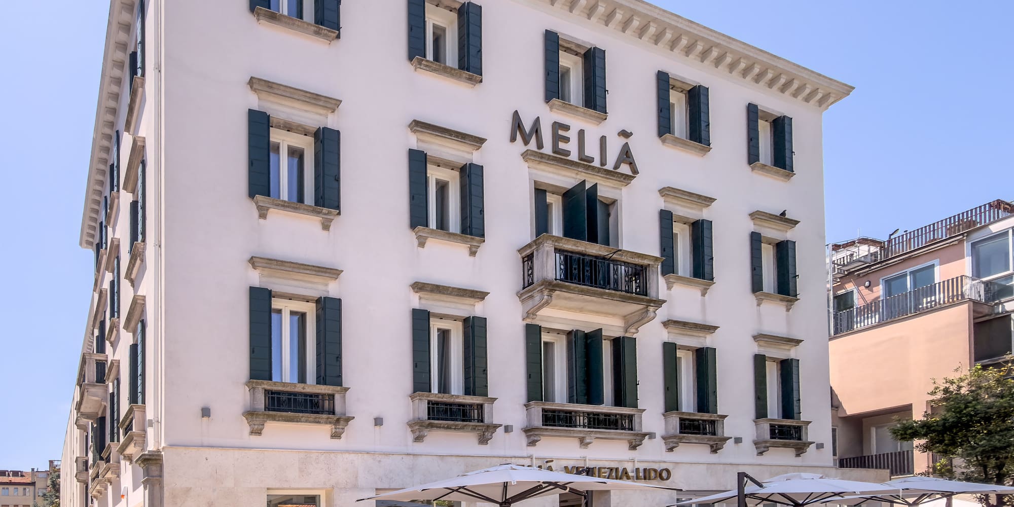 Meliá Venezia Lido hotel, white facade, green shutters, outdoor cafe.