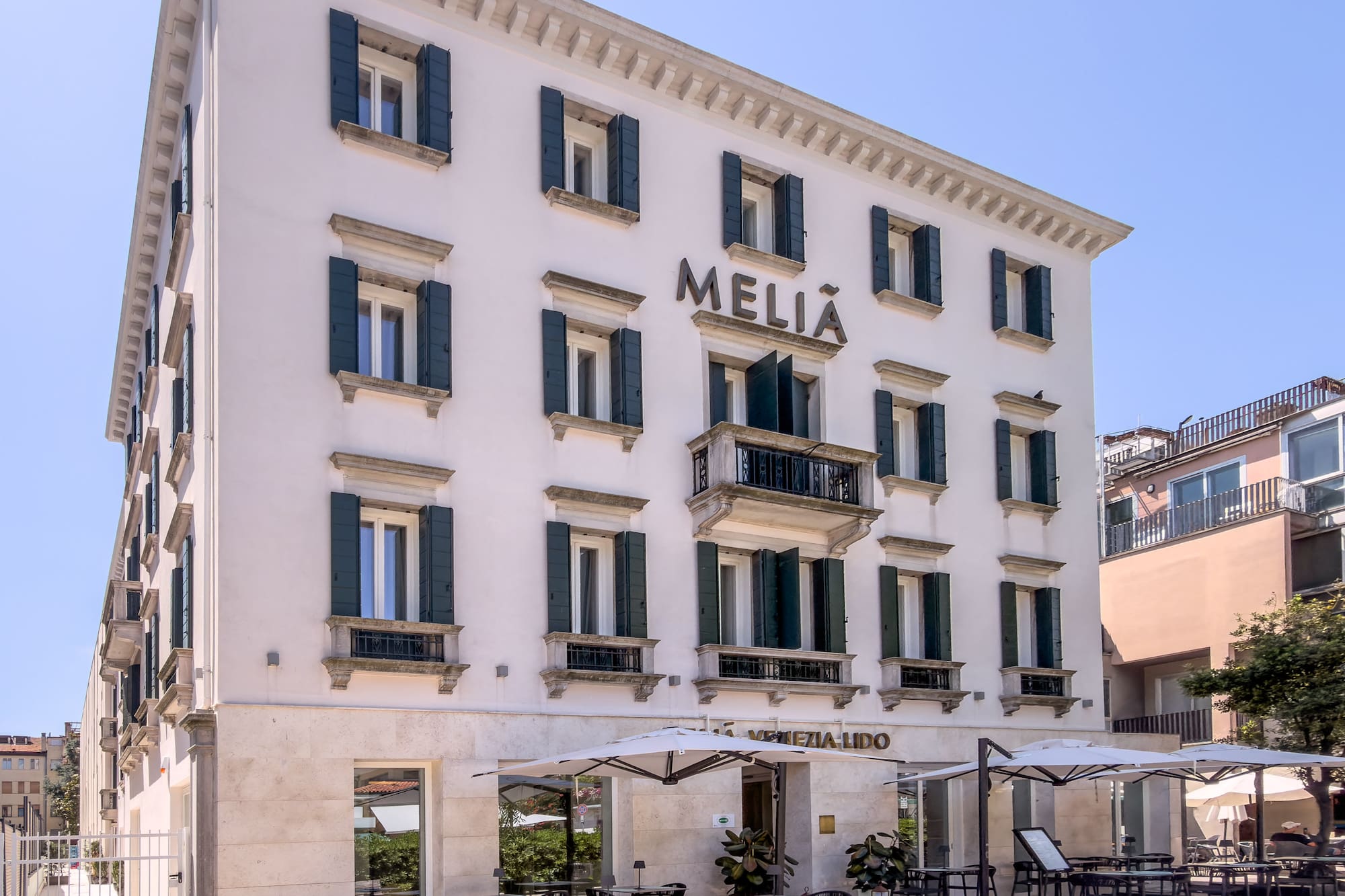 Meliá Venezia Lido hotel, white facade, green shutters, outdoor cafe.