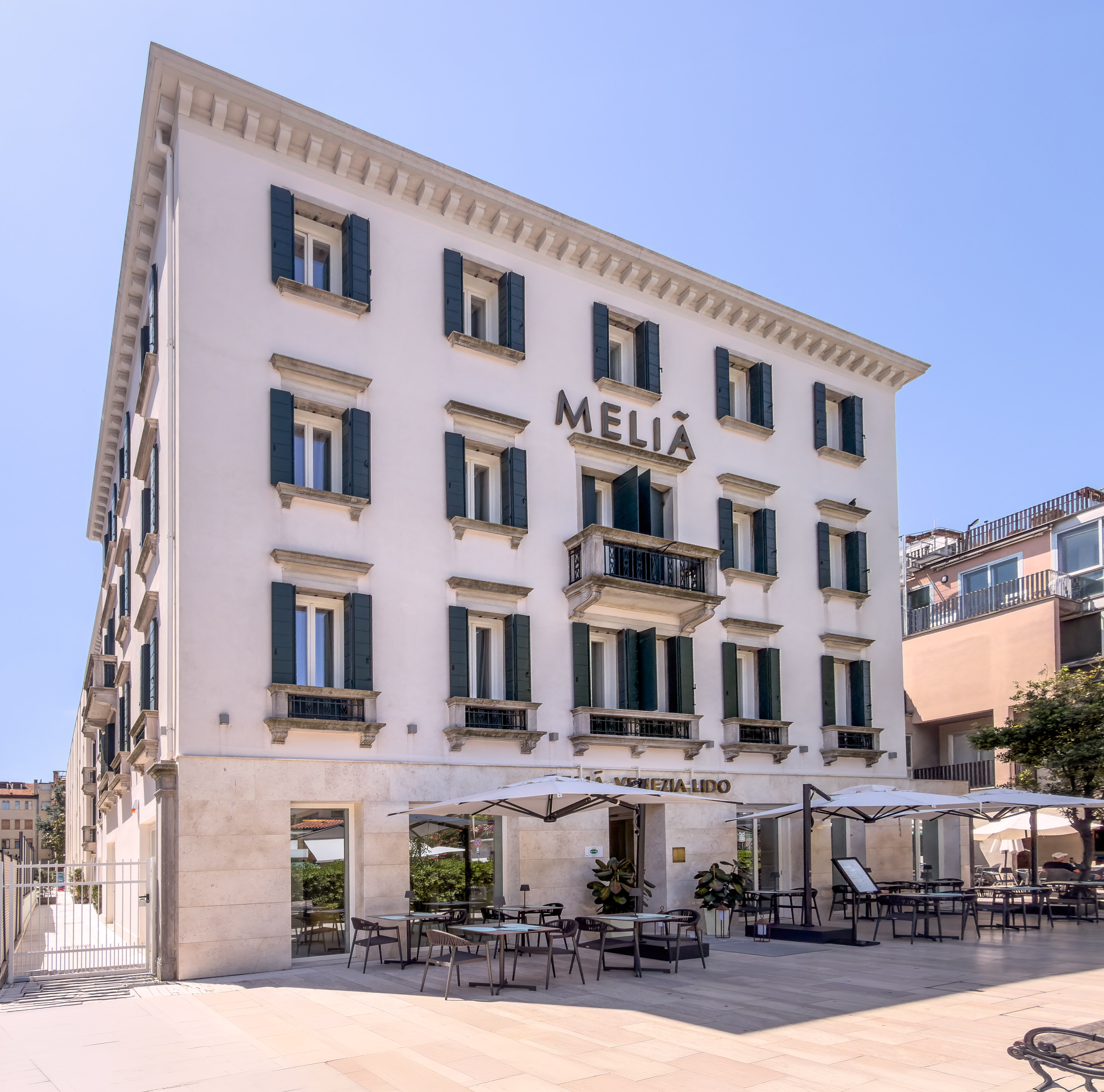 Meliá Venezia Lido hotel exterior, white building, green shutters, outdoor dining.