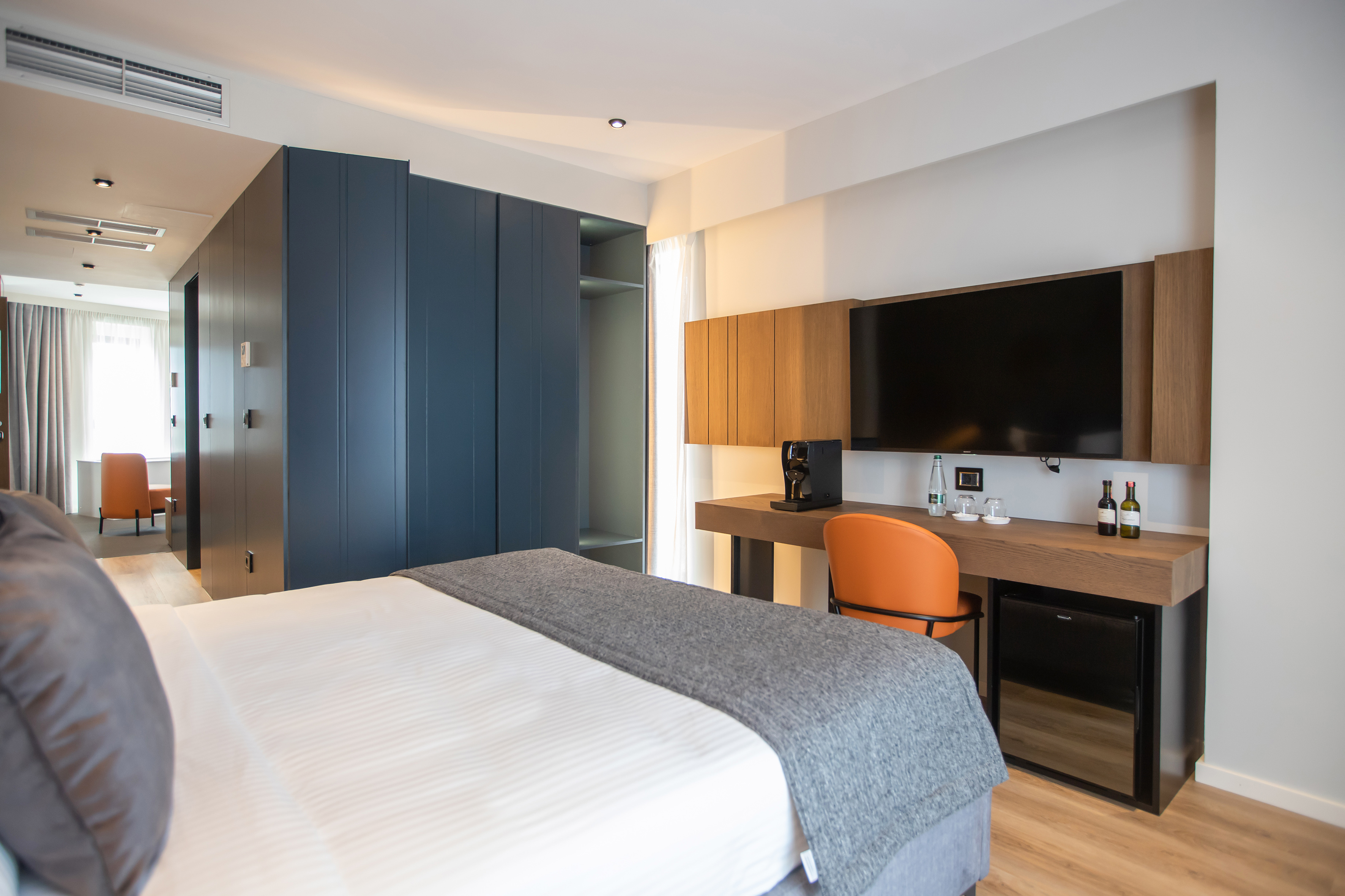 Modern hotel room with large bed, blue wardrobes, flat-screen TV, and desk.