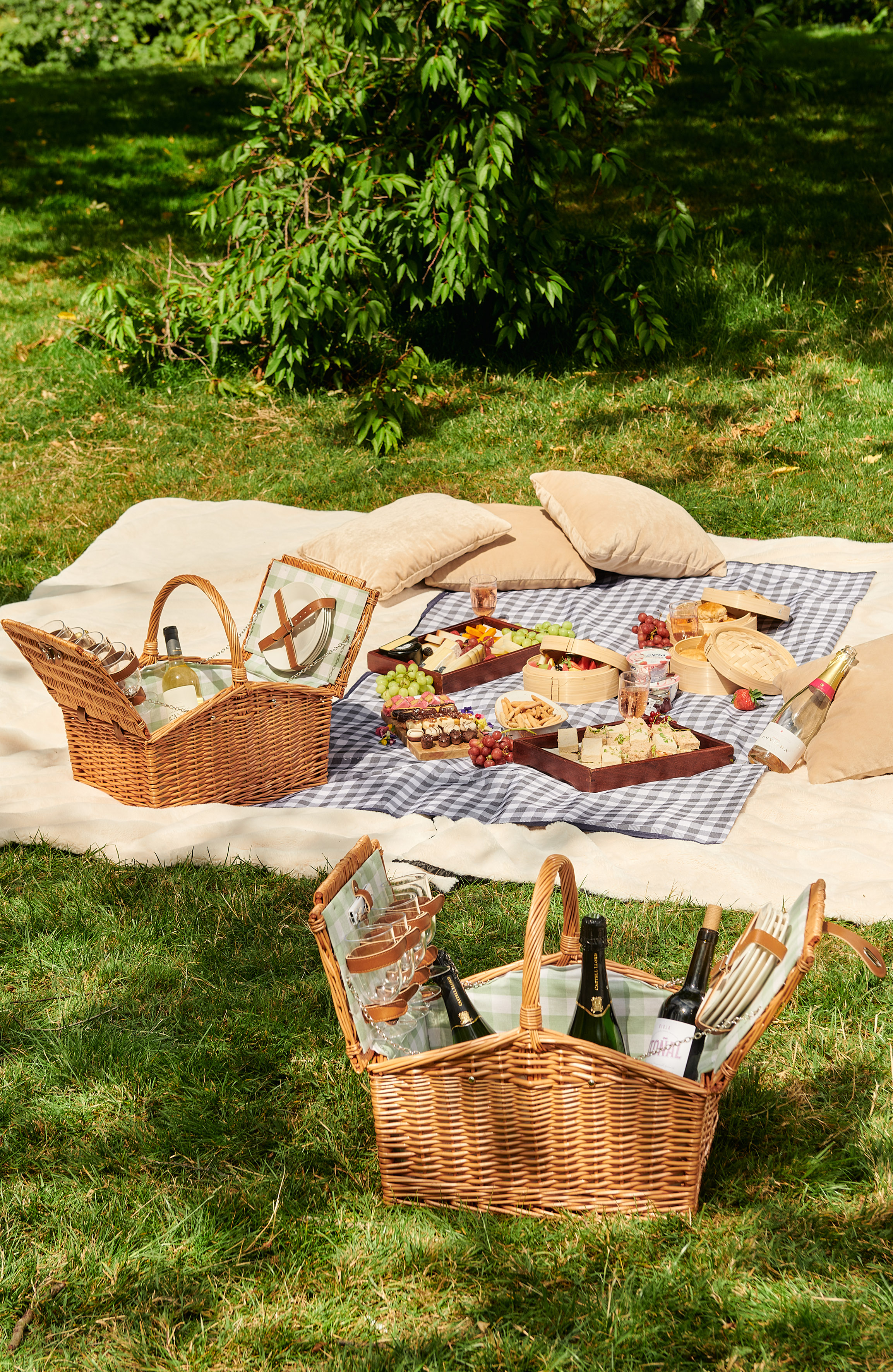 Sunny park picnic with two wicker baskets, food, wine, and blankets on grass.