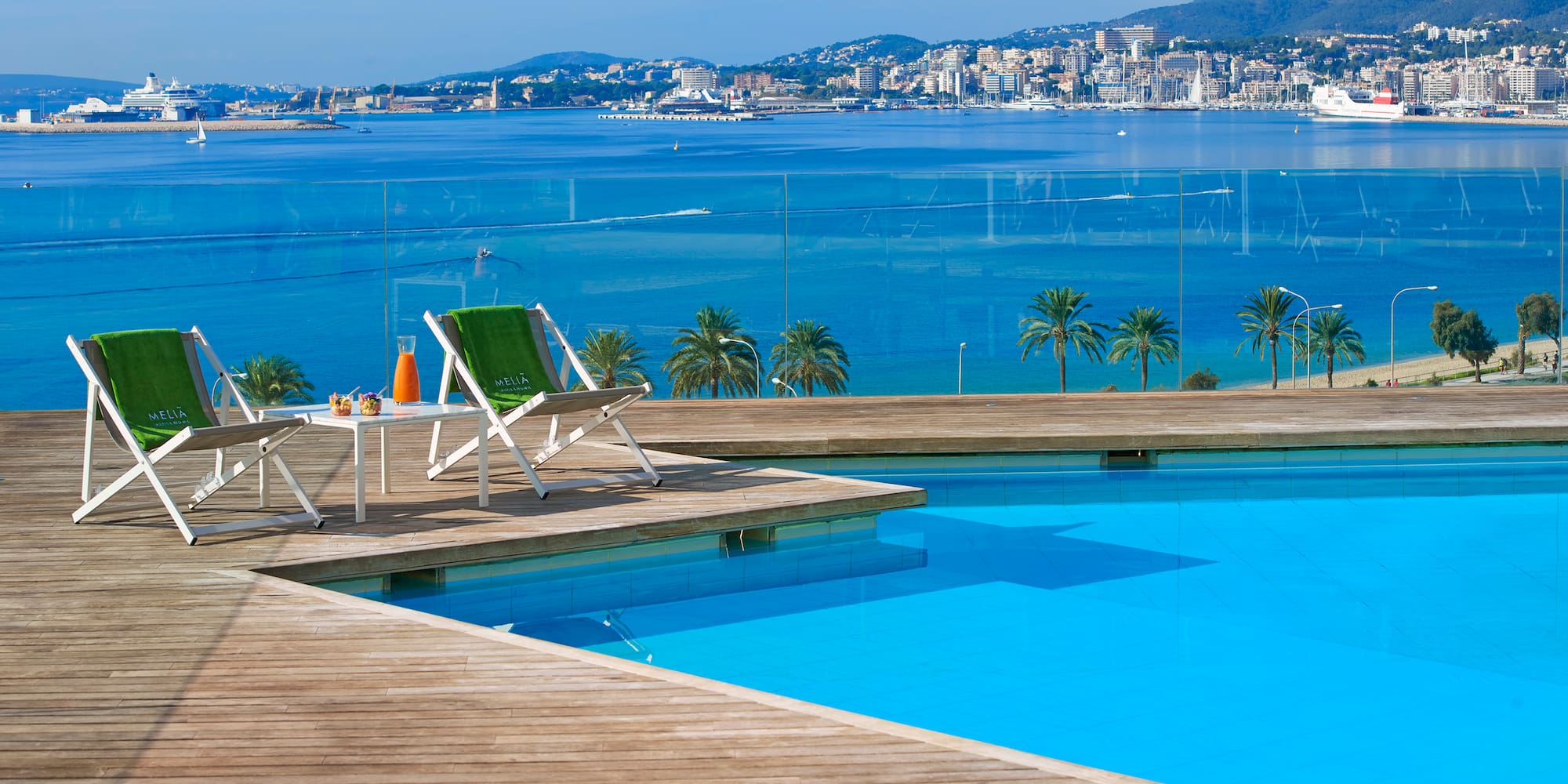 a pool with a deck and chairs and a city in the background