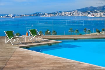 a pool with a deck and chairs and a city in the background
