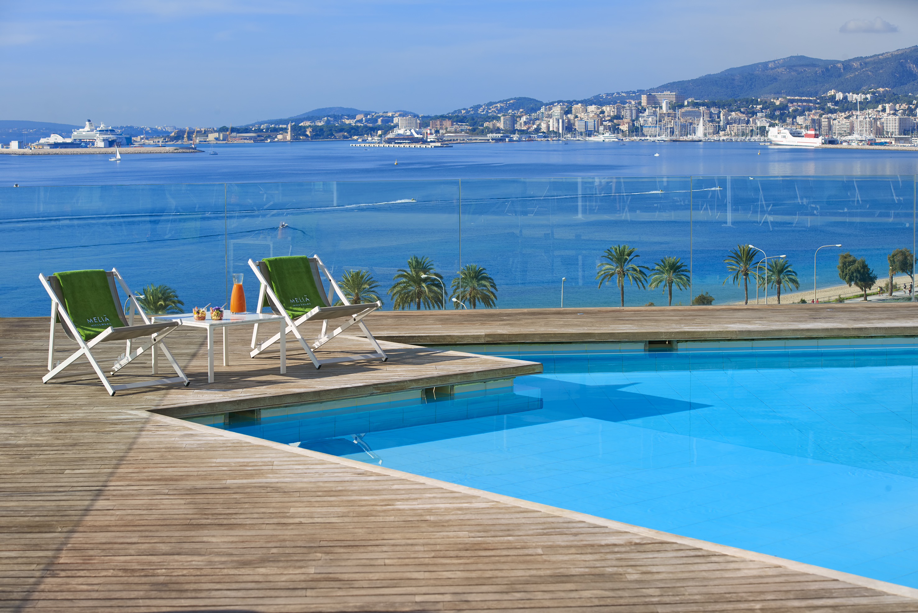 Meliã resort pool deck overlooking a sunny bay with city and ships.