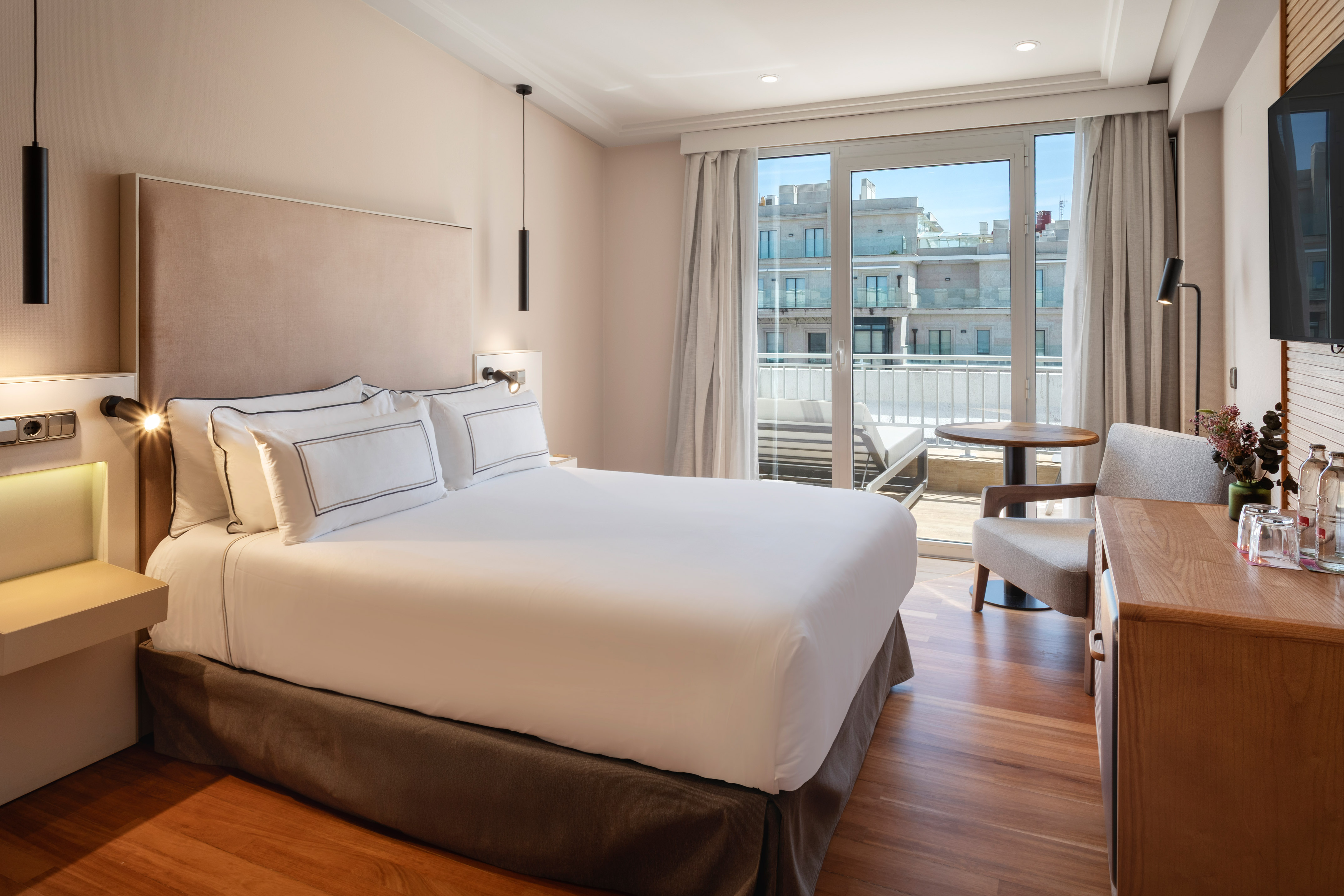 Modern hotel bedroom with a king bed, wood floor, and sunny balcony.