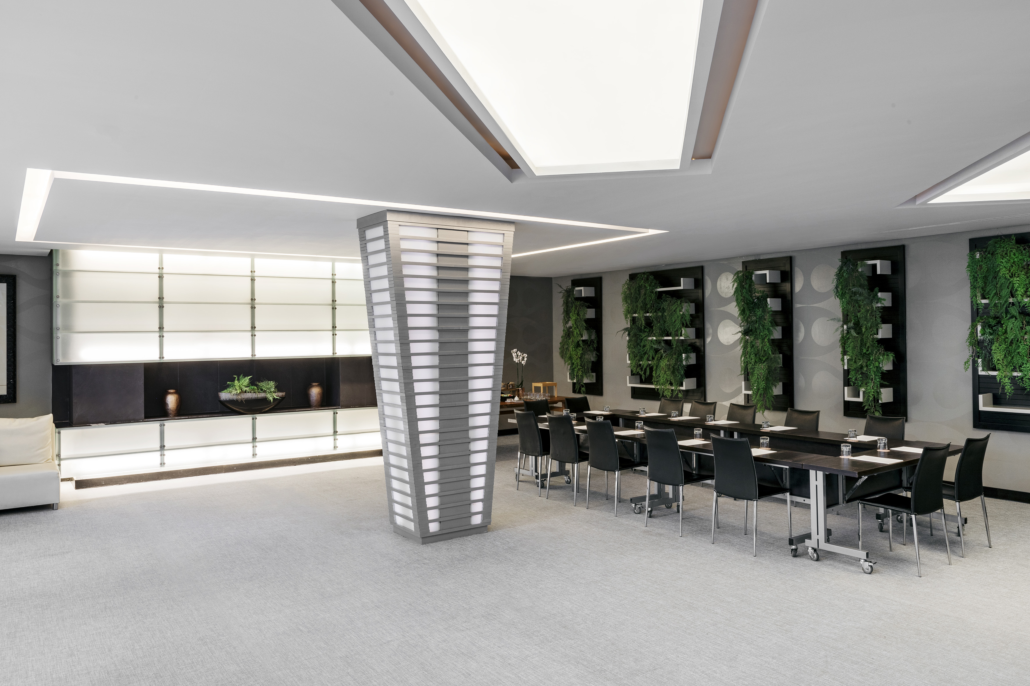 Modern conference room with dark tables, green plant walls, and sleek lighting.