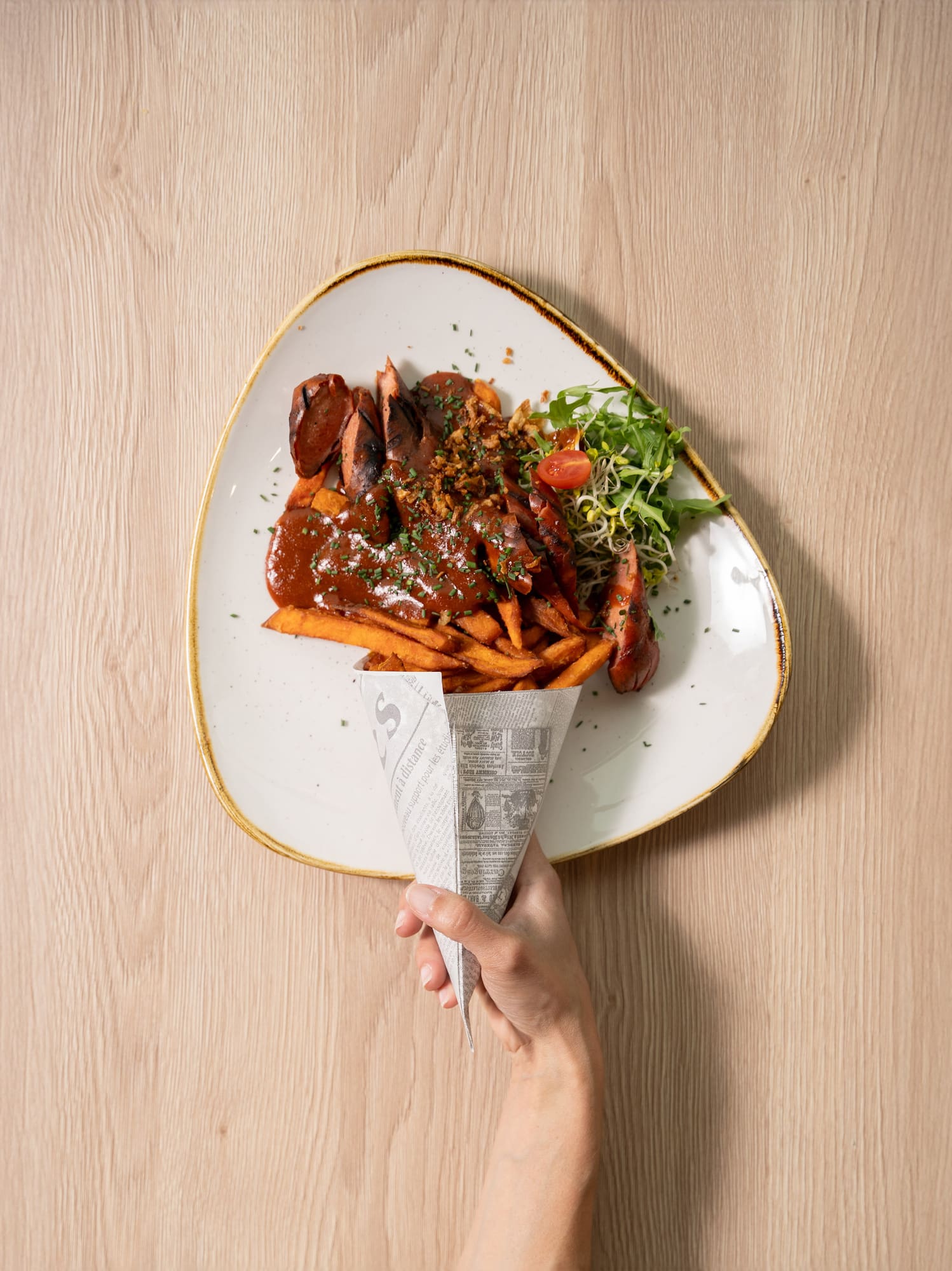 a hand holding a paper cone over a plate of food