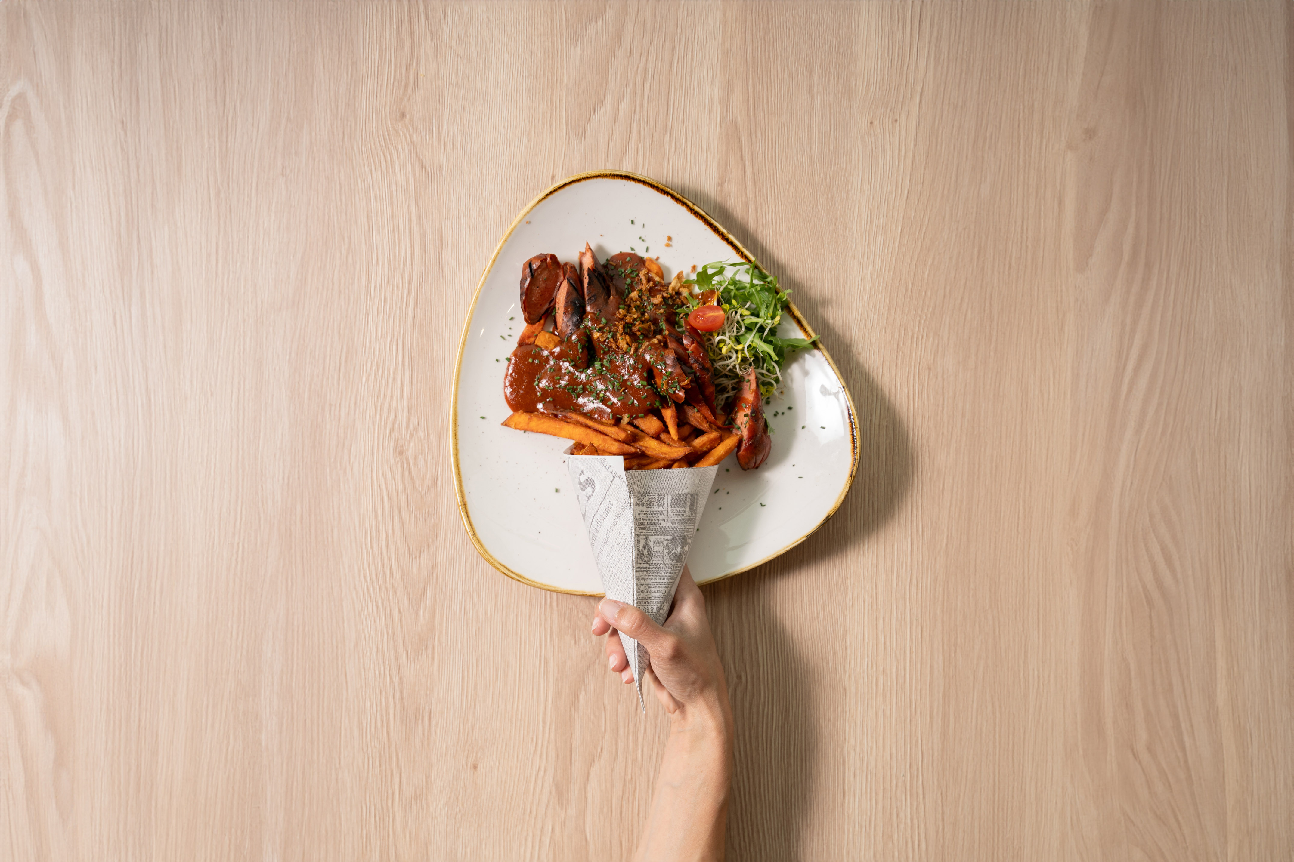 Currywurst with sweet potato fries, rich sauce, and fresh salad on a modern plate.