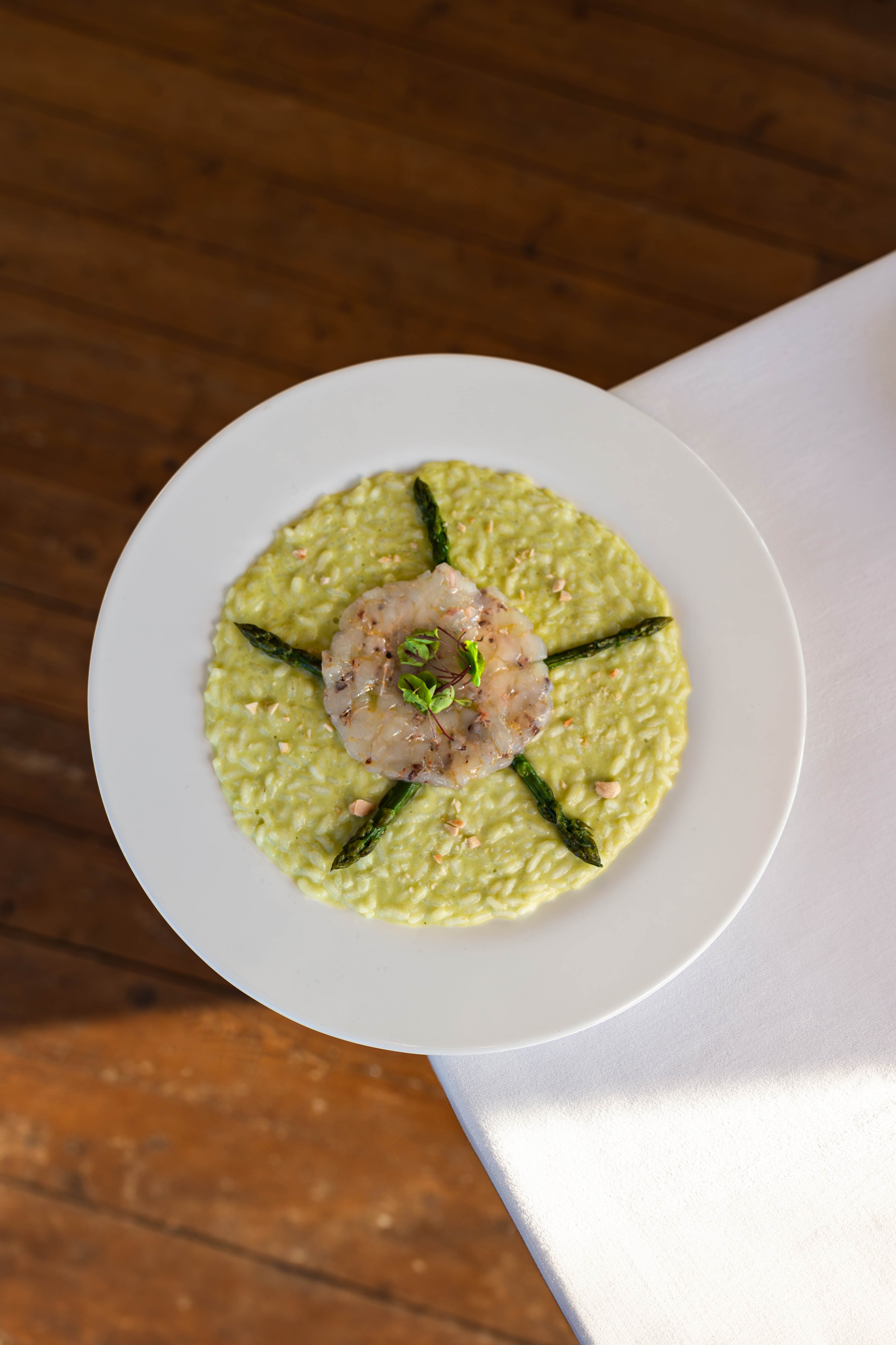Green risotto with seared white fish, asparagus, and microgreens on white plate.