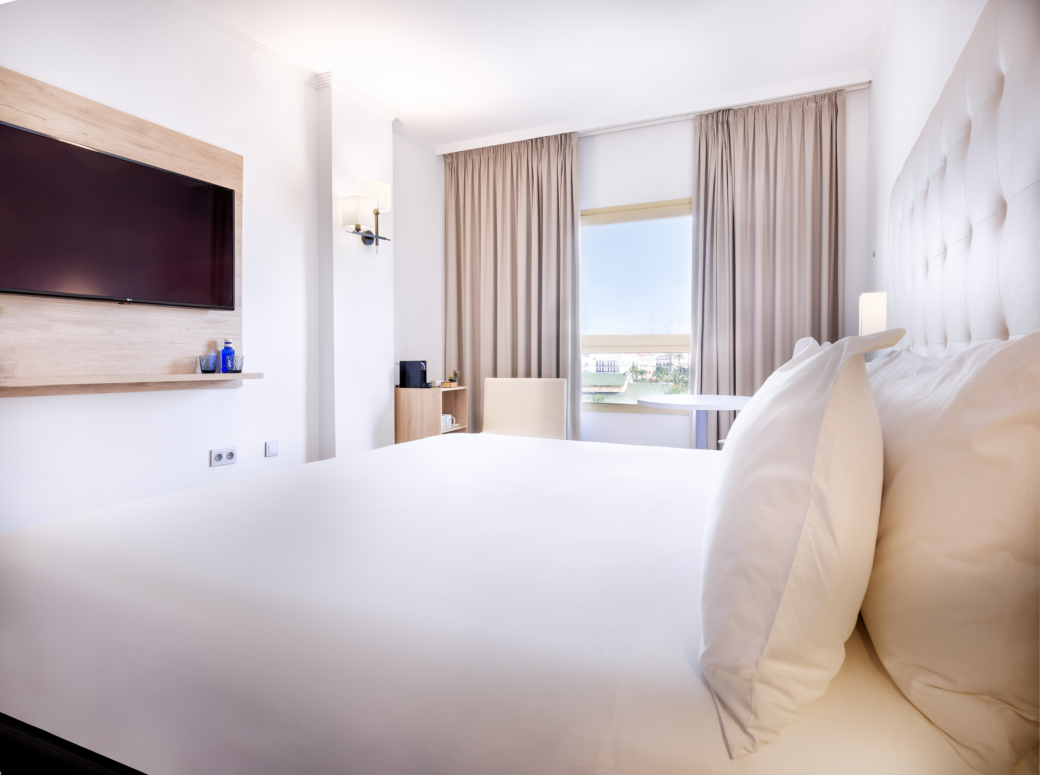 a bed with white sheets and a tv on the wall