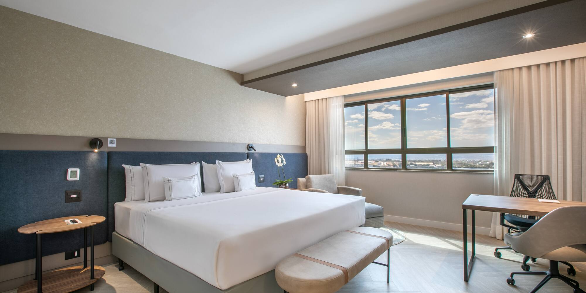 Modern hotel room with king bed, work desk, and window city view.