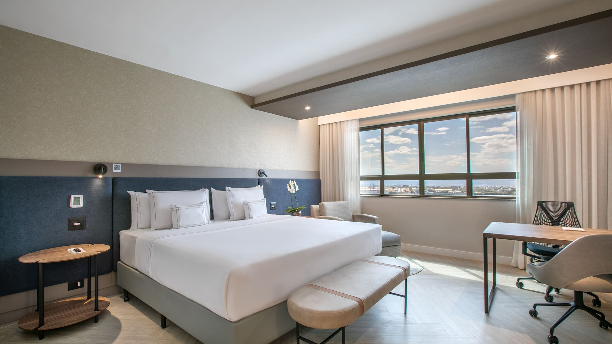 Modern hotel room with king bed, work desk, and window city view.