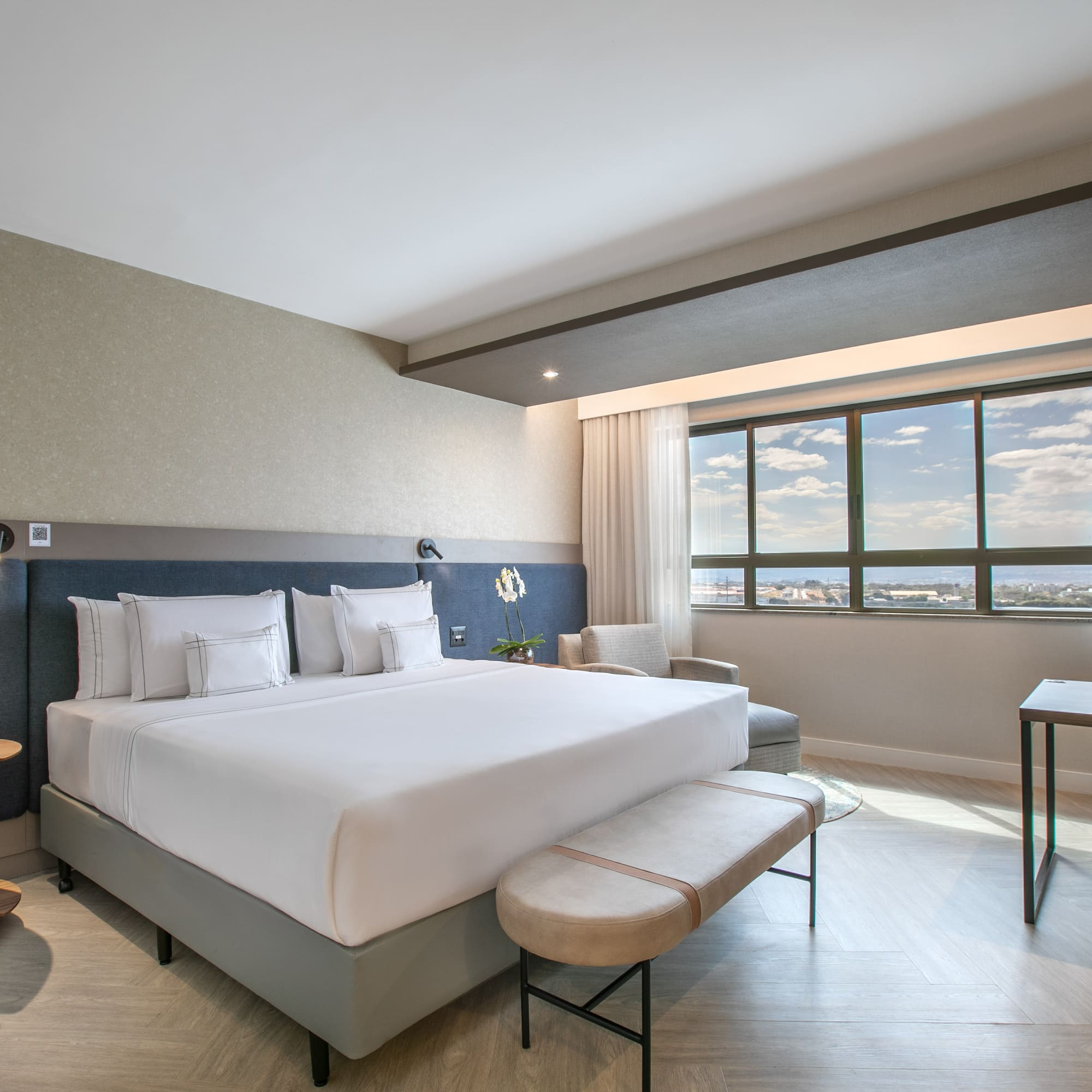Modern hotel room with king bed, workstation, and city view.