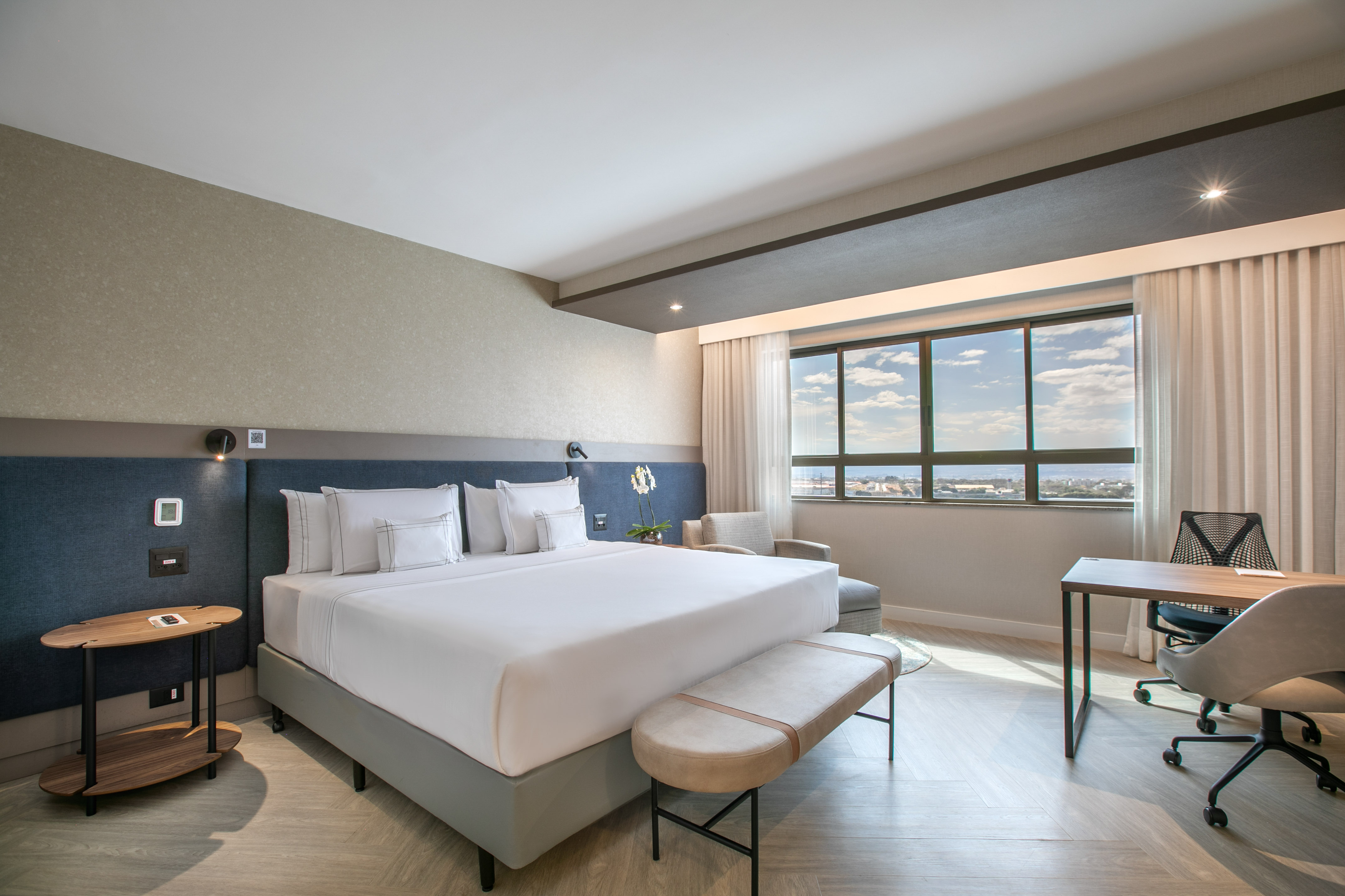 Modern hotel room with king bed, workstation, and city view.