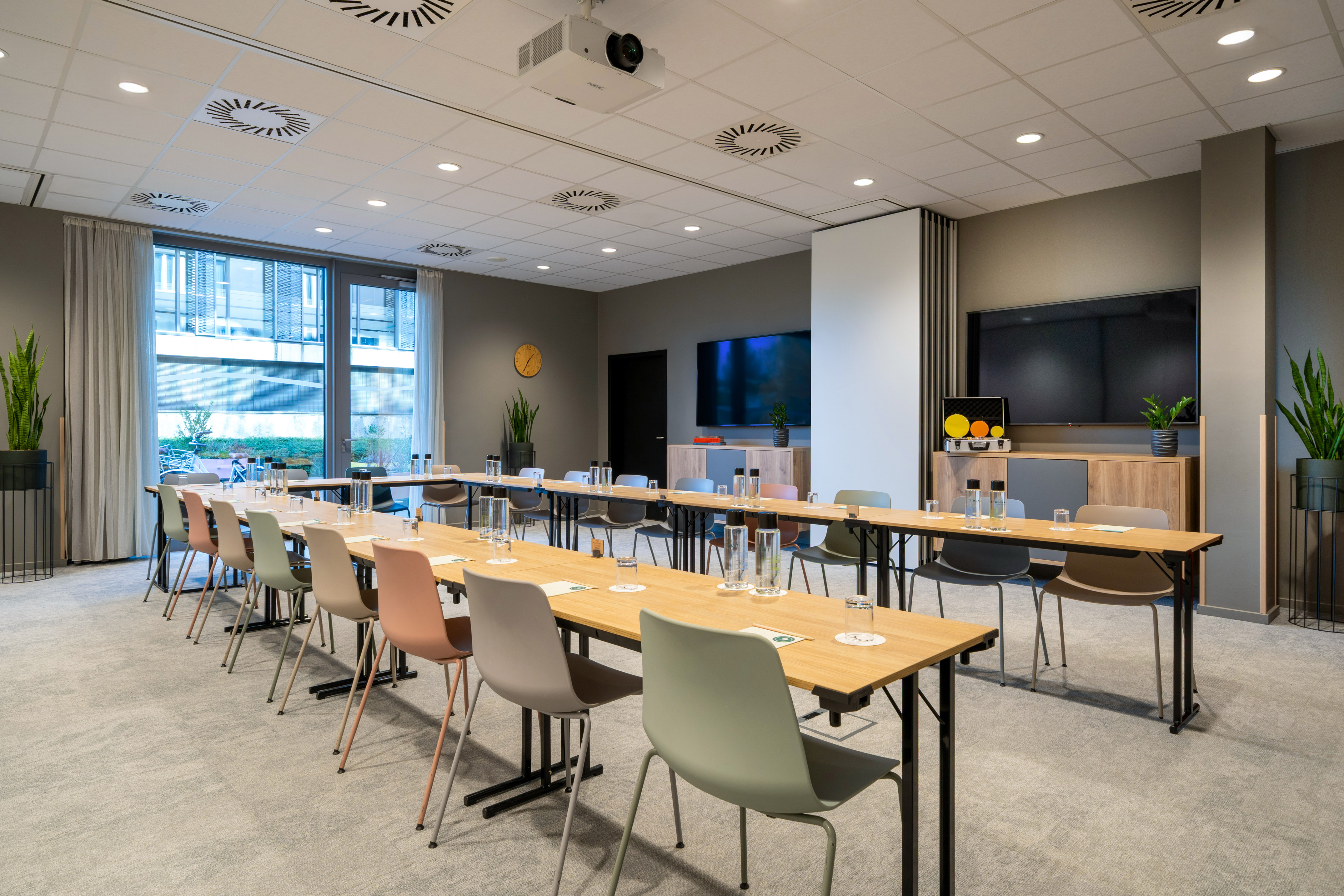 Modern U-shaped conference room with colorful chairs, projector, and large TV screen.