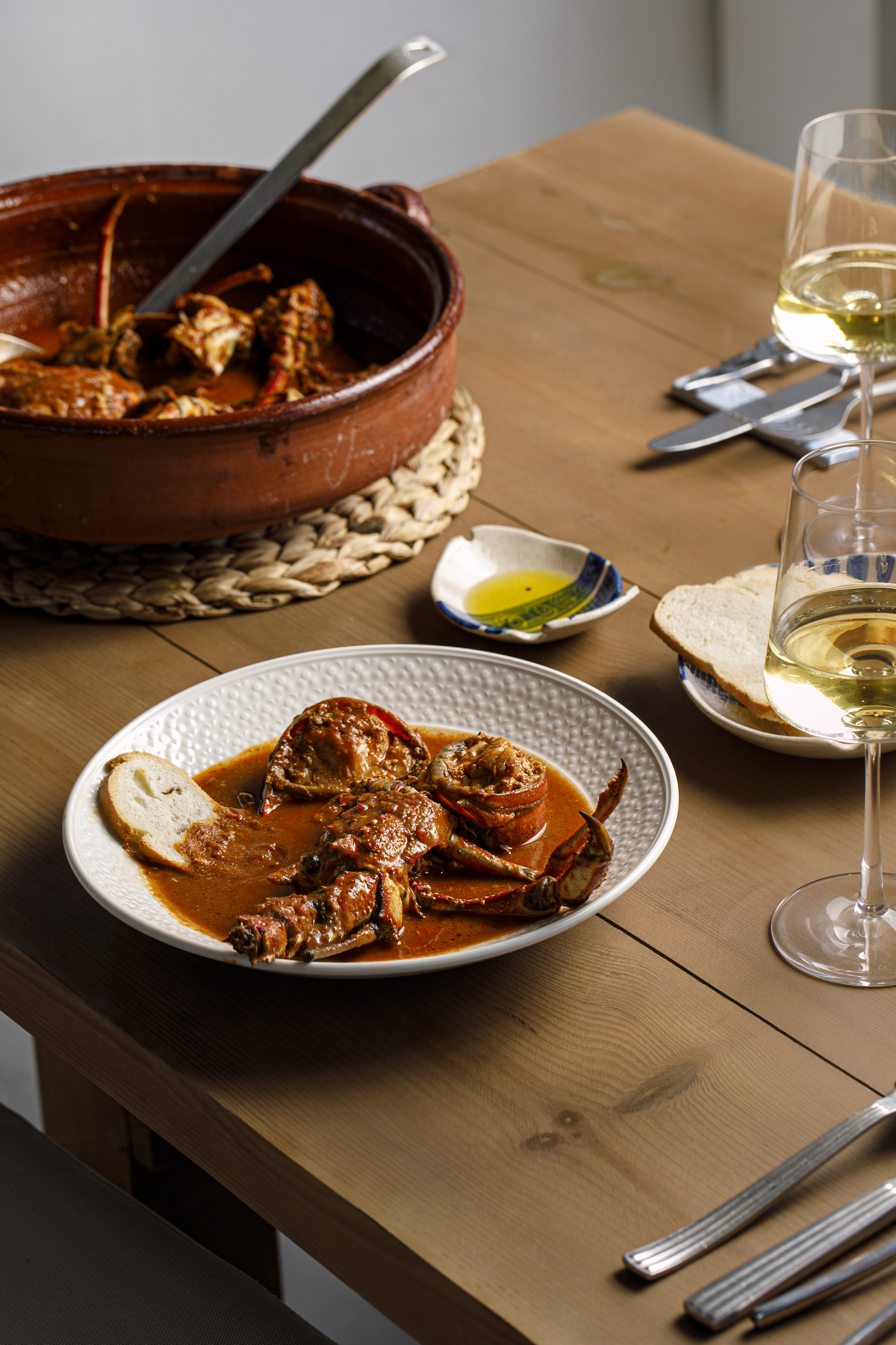 Rustic crab stew in a rich red sauce, bread, and white wine served on wood.