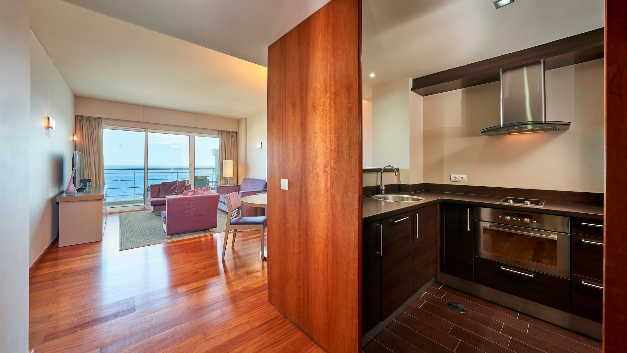 Apartment living room with sea view and adjacent modern kitchenette.