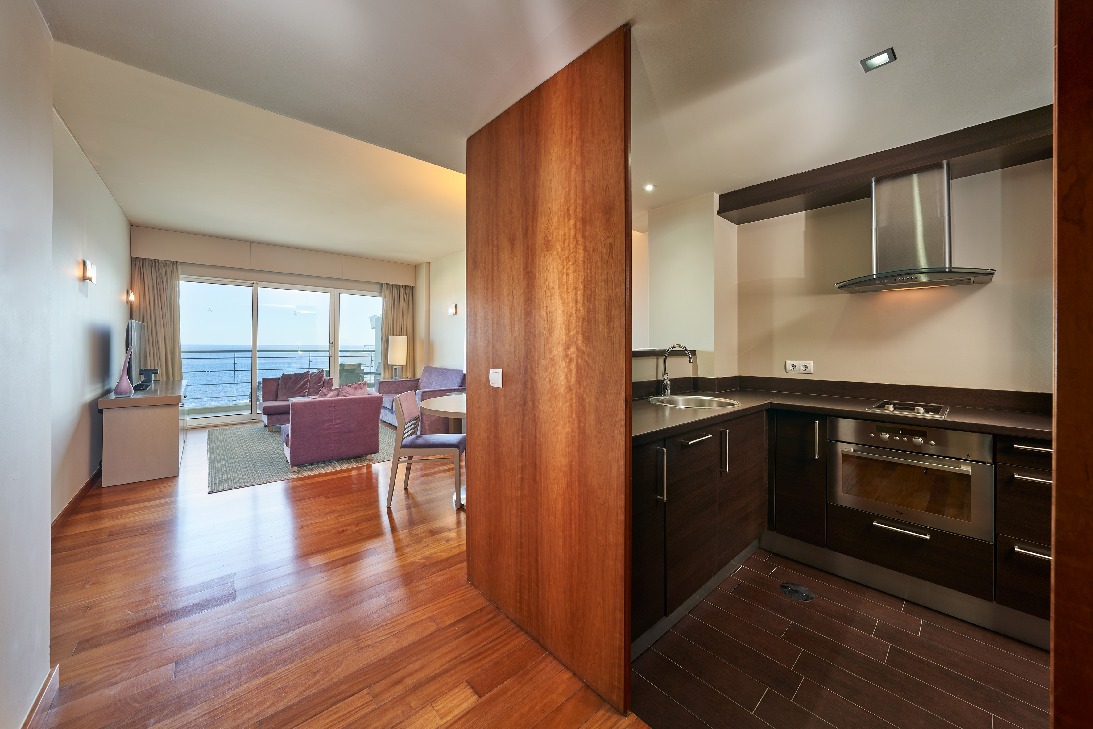 Apartment living room with sea view and adjacent modern kitchenette.