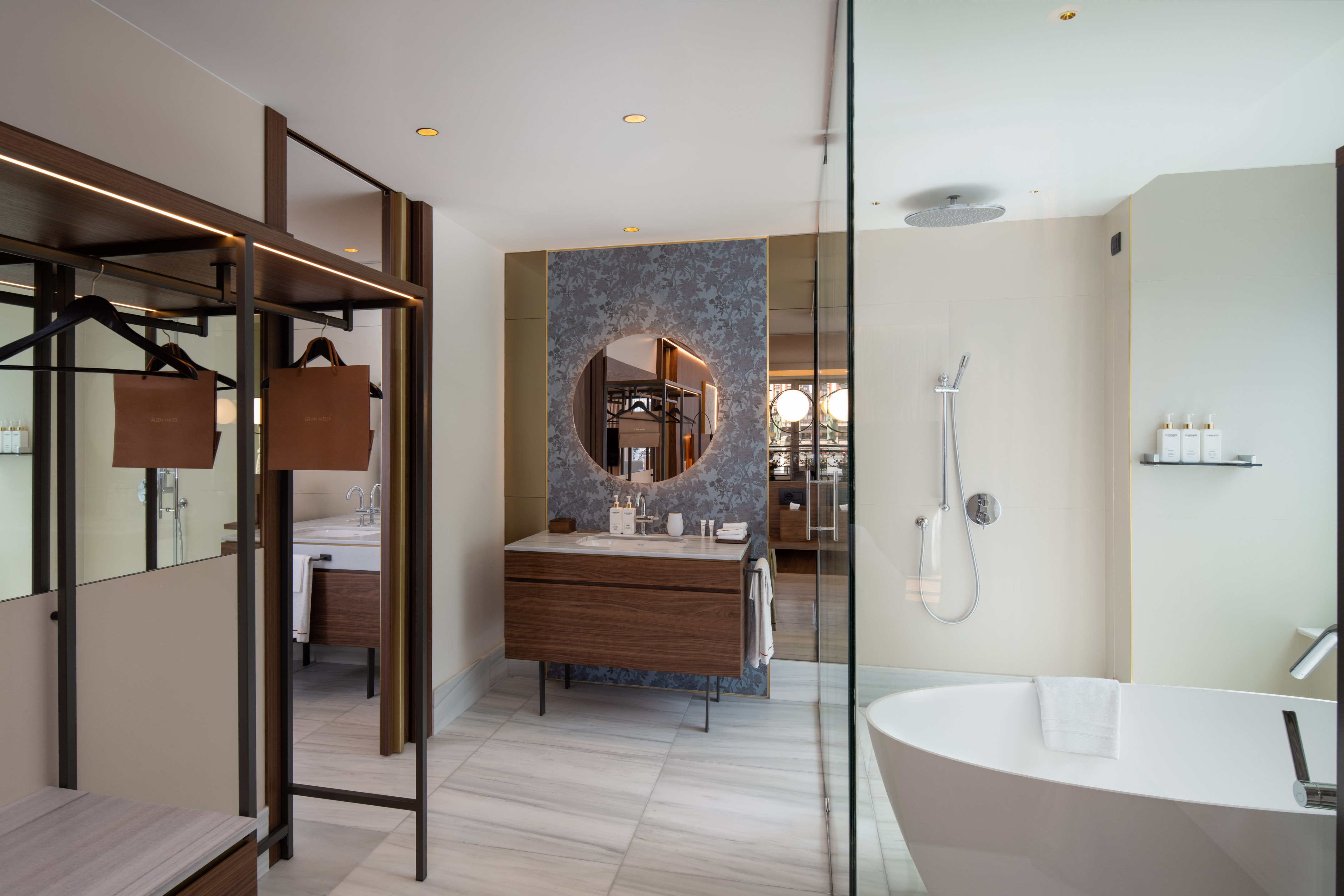 Modern hotel bathroom with walk-in shower, freestanding tub, wood vanity, marble.