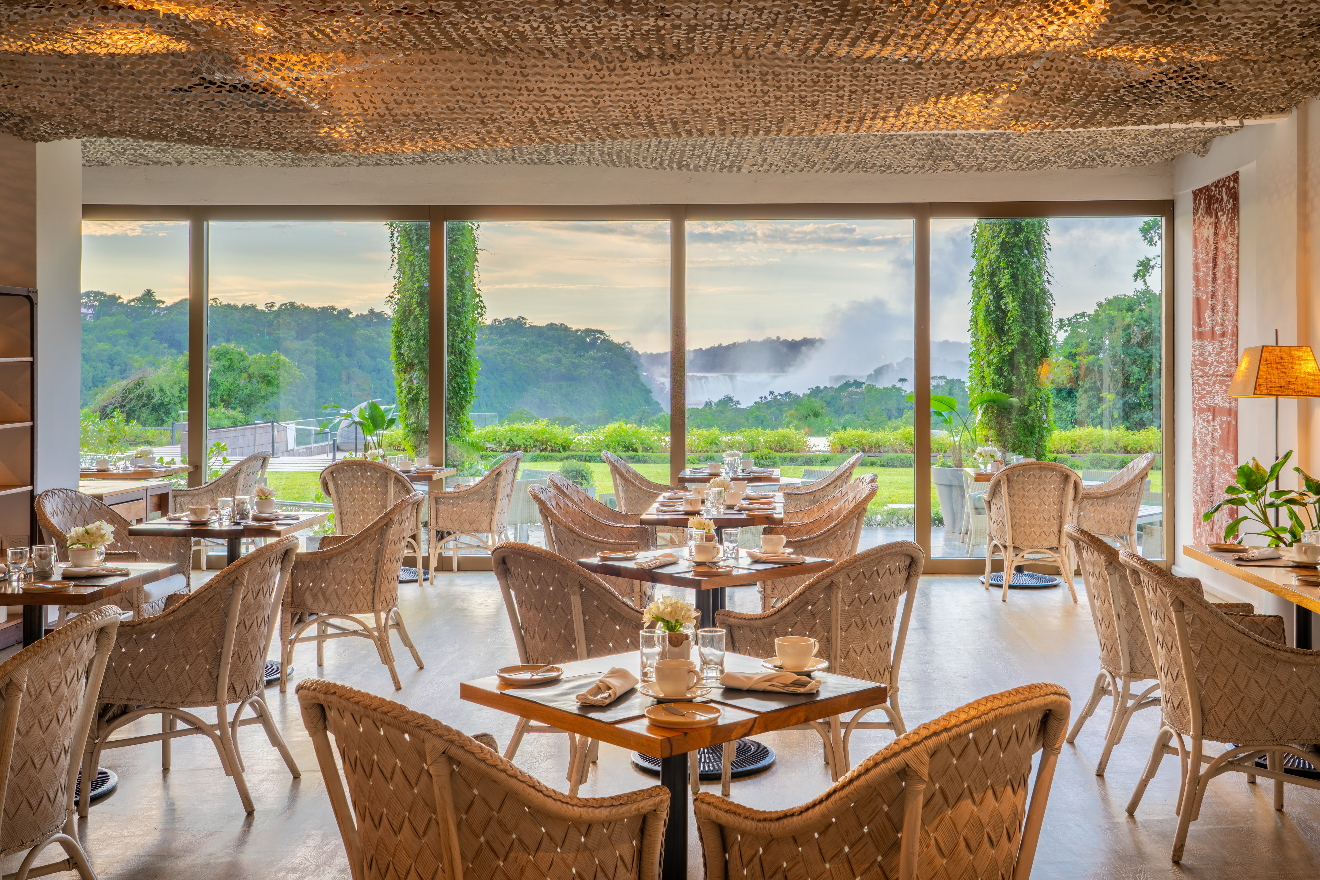 Hotel restaurant with Victoria Falls view, set tables, and wicker chairs.