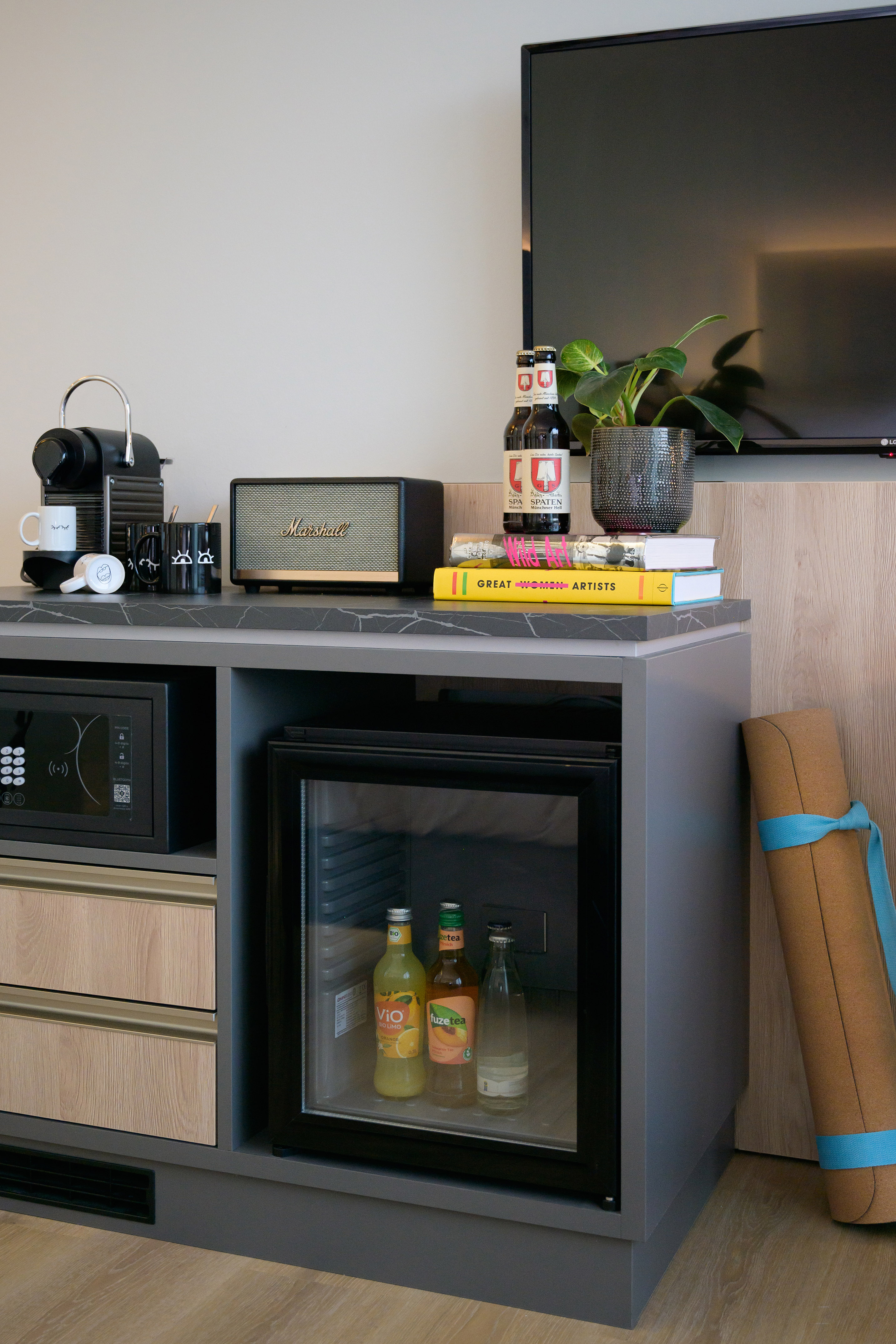 Modern hotel minibar: Nespresso, Marshall speaker, TV, safe, drinks, yoga mat.
