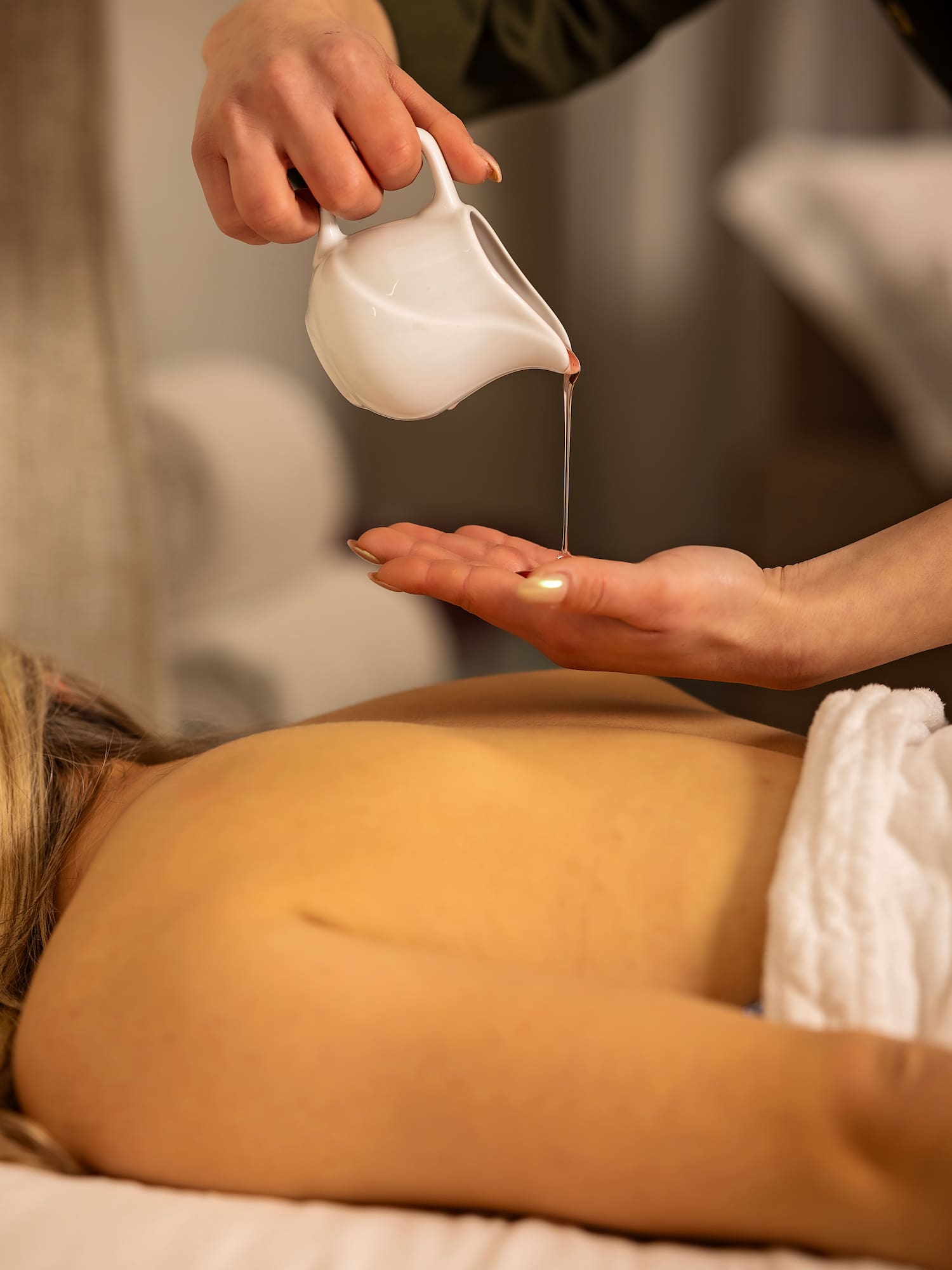Spa therapist pouring warm oil onto hand for a relaxing back massage.
