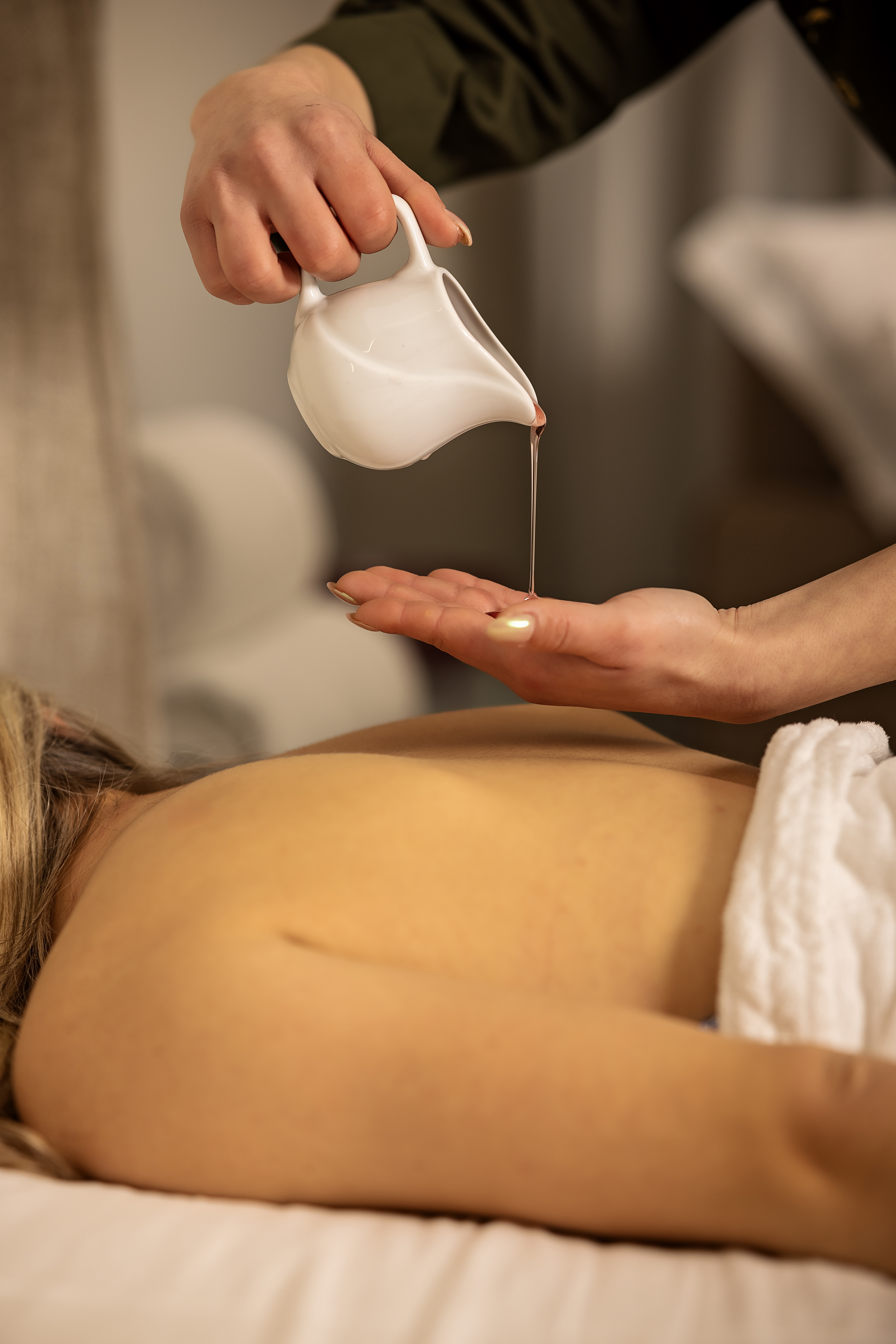 Spa therapist pouring warm oil onto hand for a relaxing back massage.