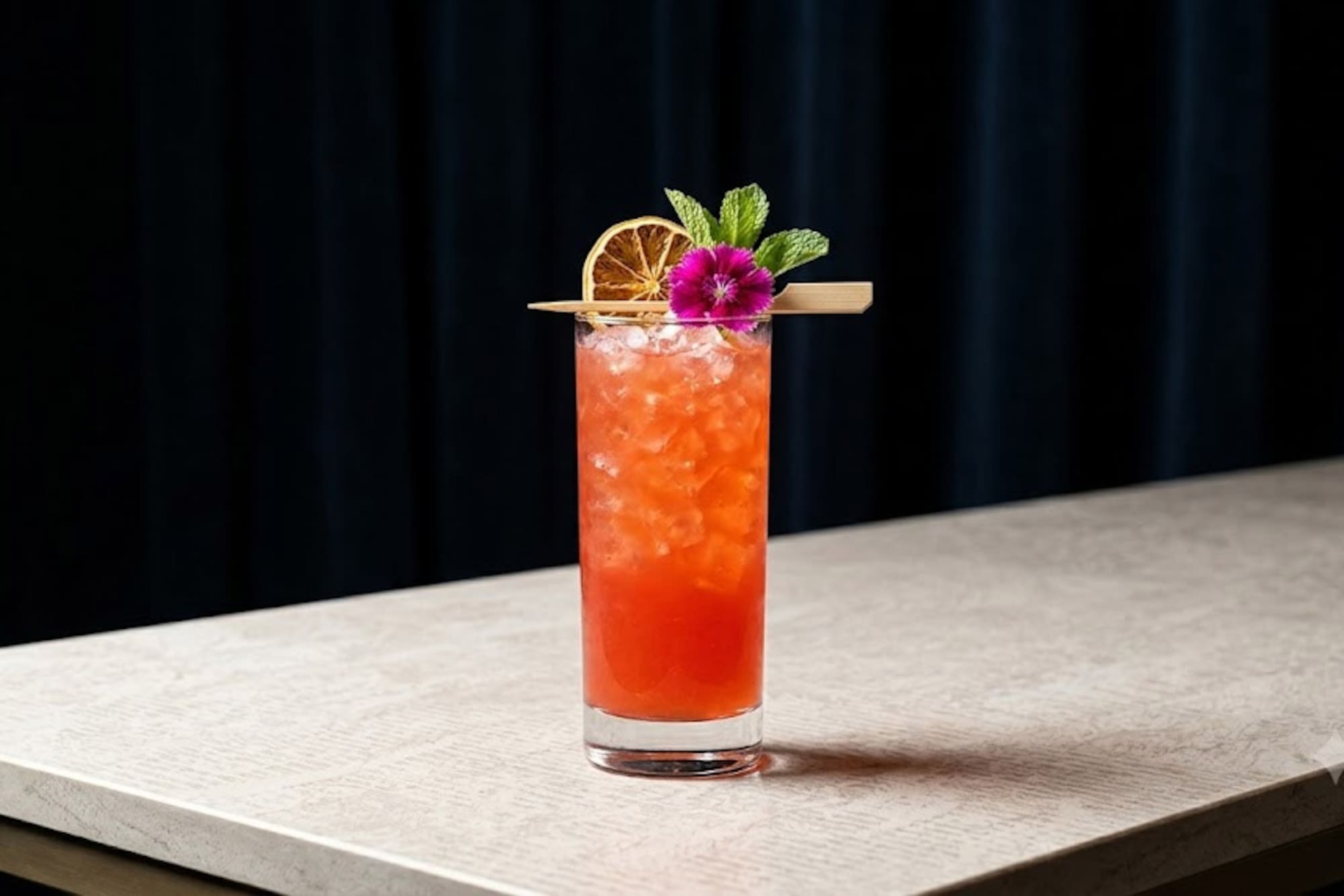 Colorful highball cocktail with ice, dried orange, mint, and flower garnish.
